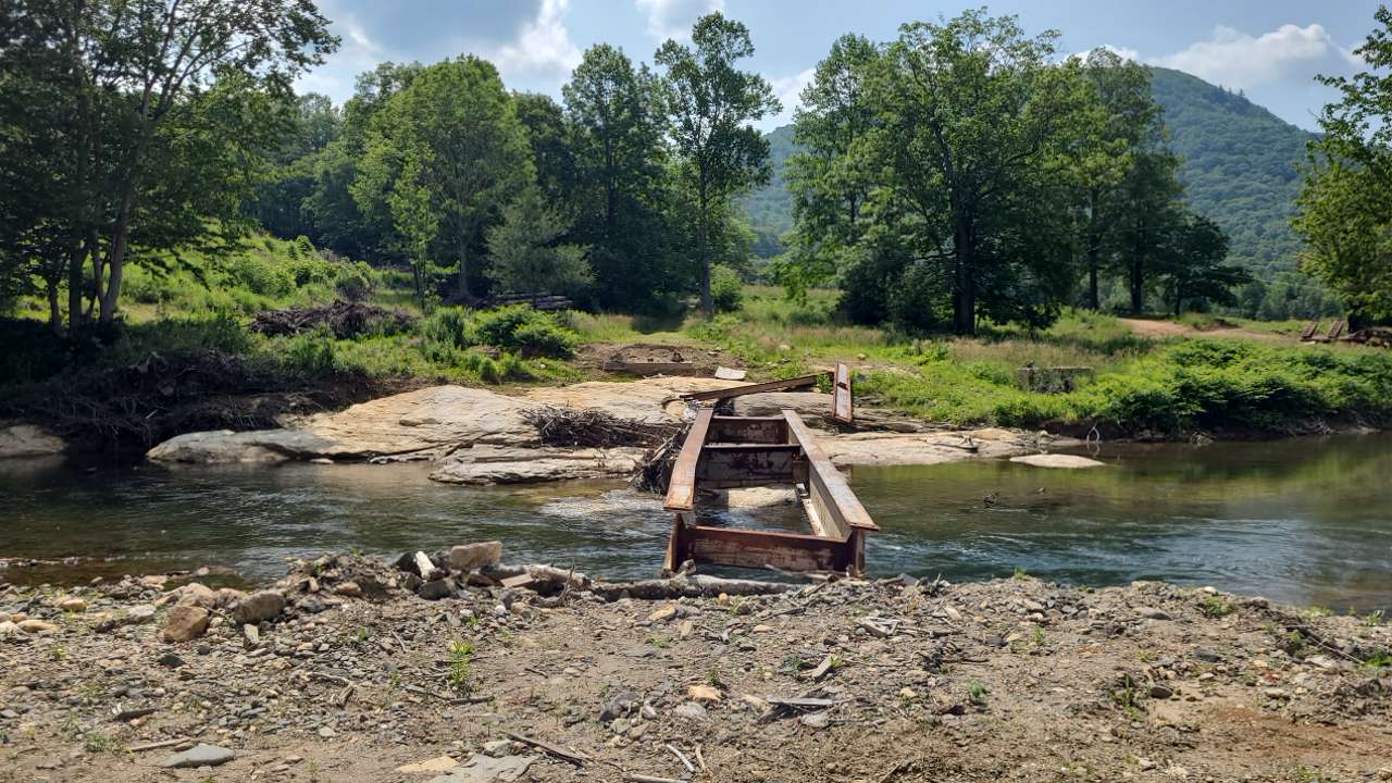 Rusty metal bridge ruins over a stream surrounded by lush trees