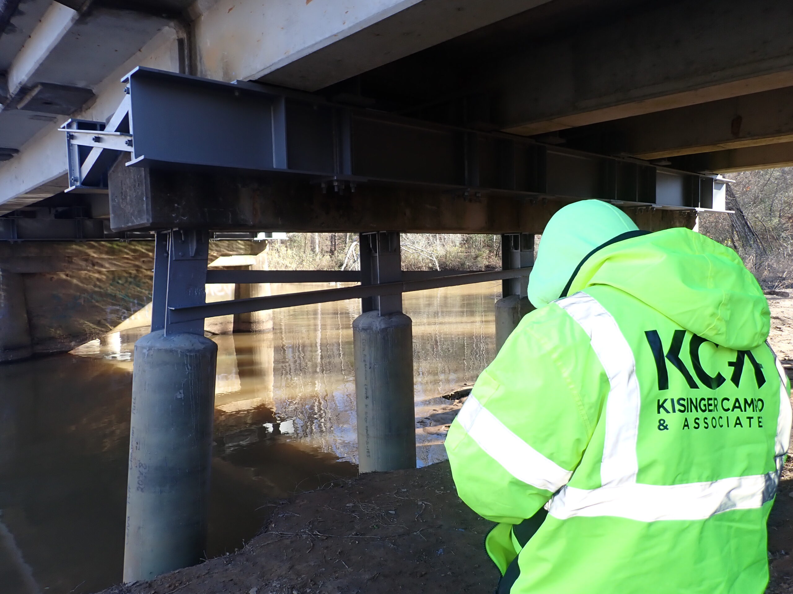 Person inspecting bridge structure, wearing Kisinger Campo & Associates jacket