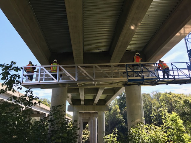 Workers in safety vests inspecting structural elements beneath a large bridge
