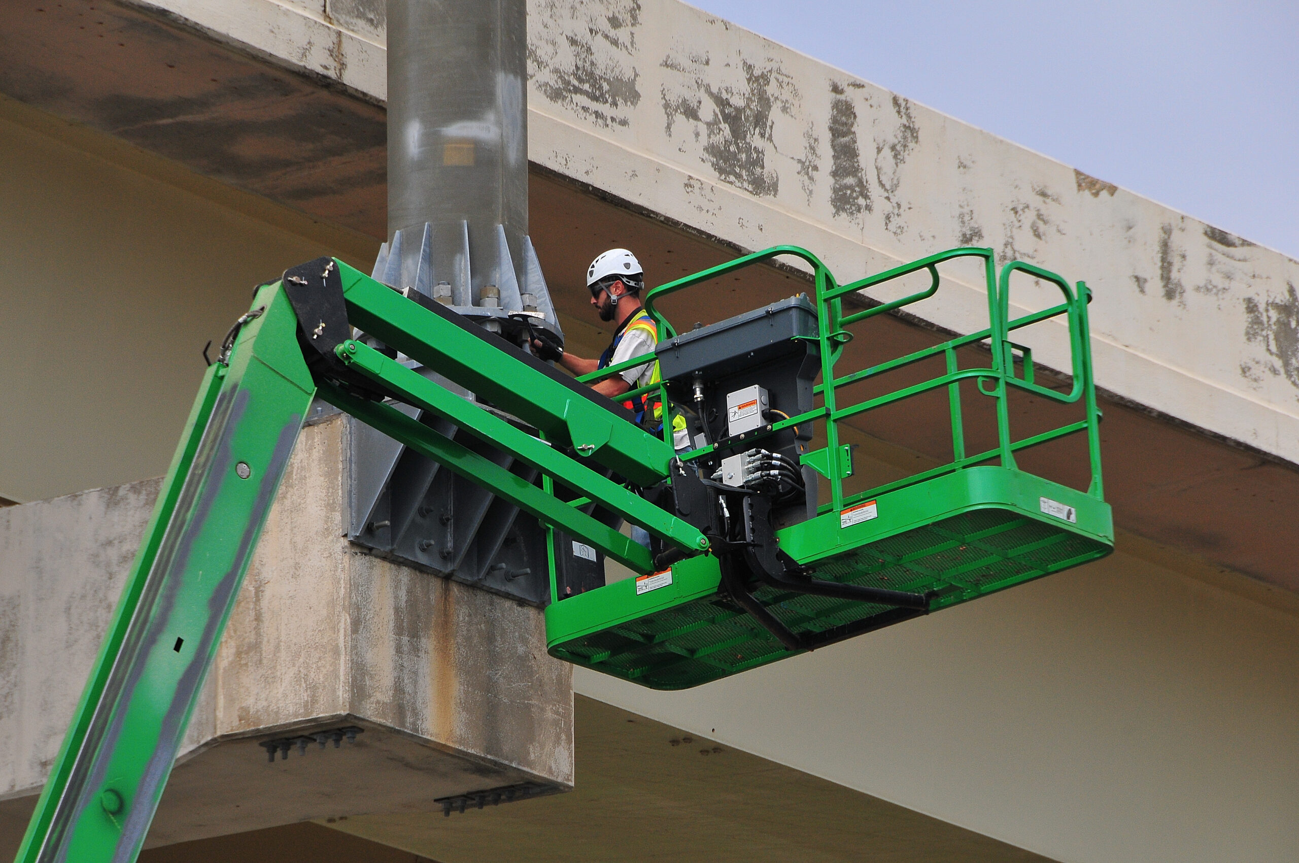 Construction worker on a green lift inspecting a concrete bridge