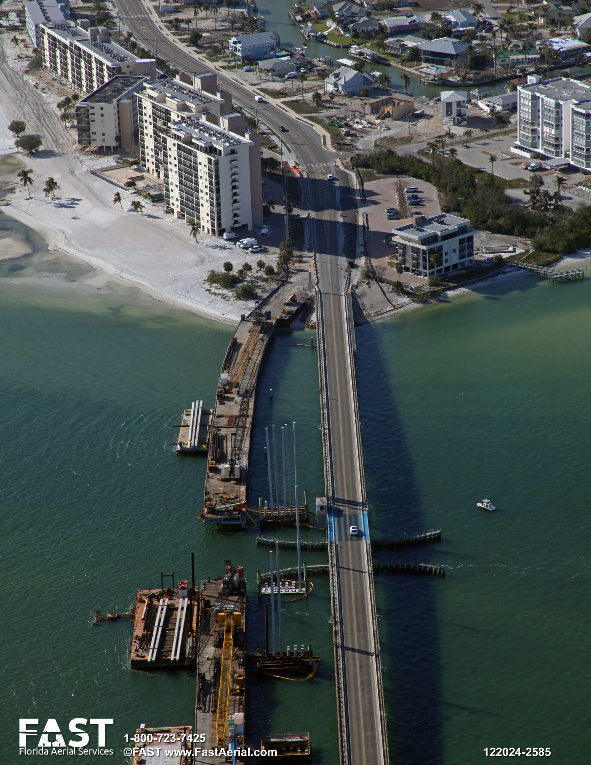 Aerial view of Estero Boulevard bridge under construction, with adjacent buildings and a boat in the water