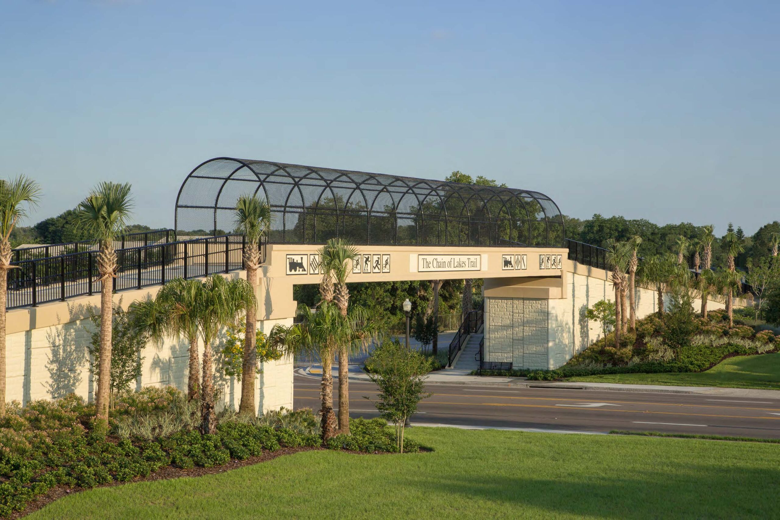 Chain of Lakes Trail bridge with decorative railings over a road, surrounded by palm trees and greenery