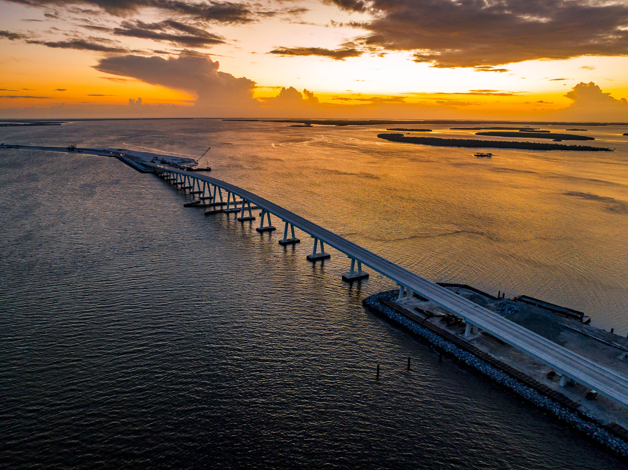 Sunset view of a bridge extending over shimmering water, capturing vivid orange skies