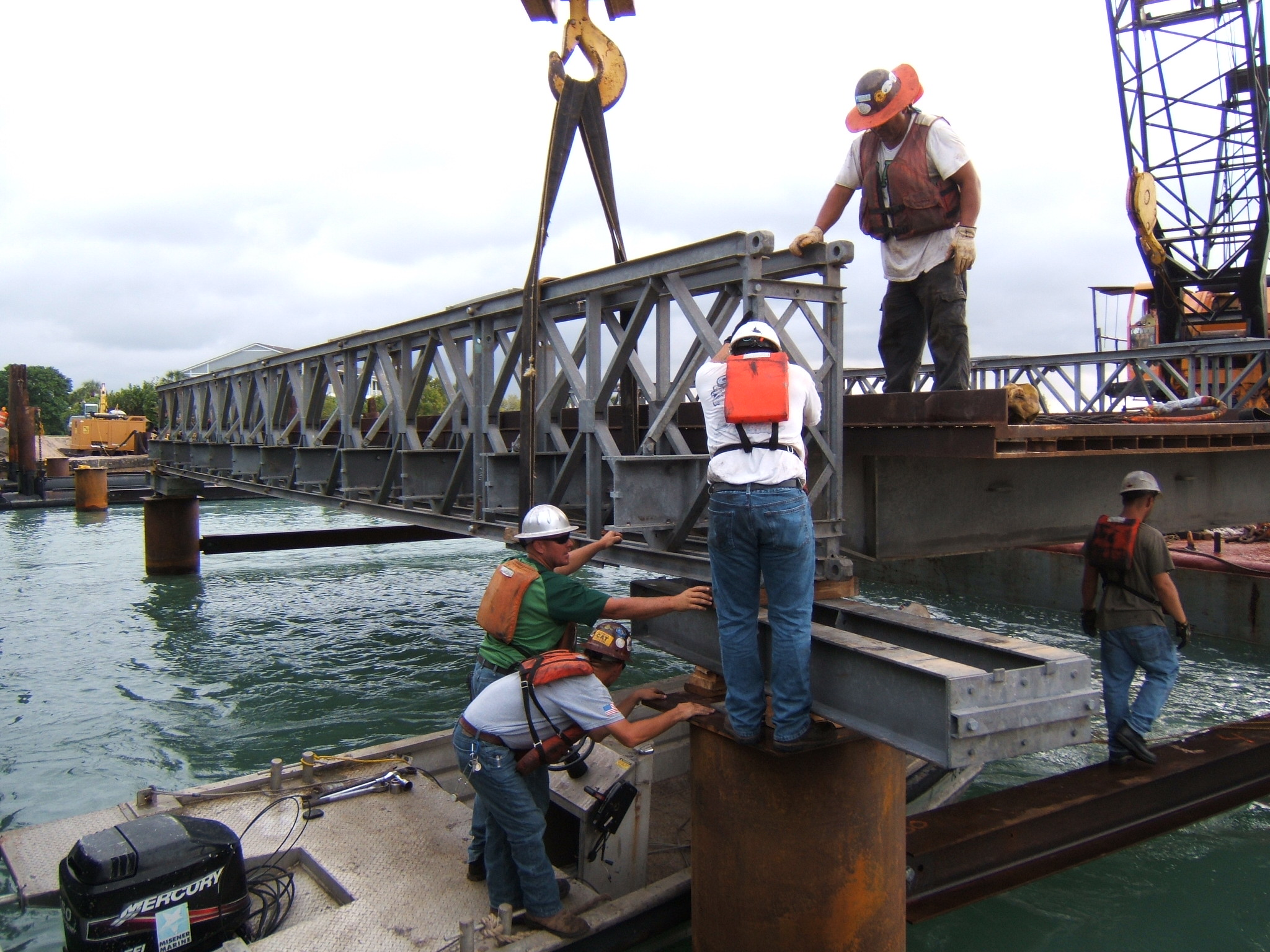Workers in safety gear positioning bridge section over water using a crane