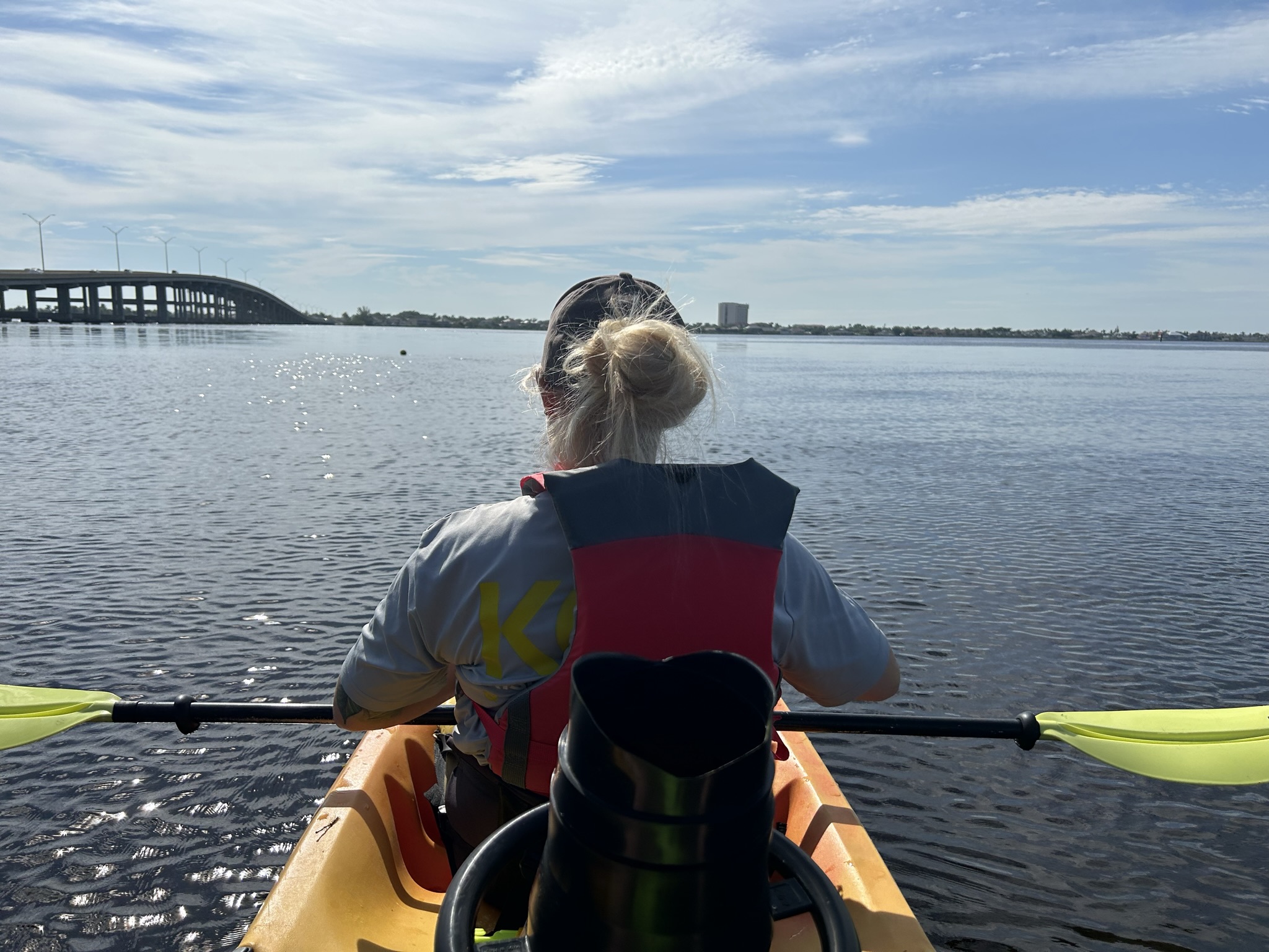 Person kayaking on calm water under clear sky near bridge