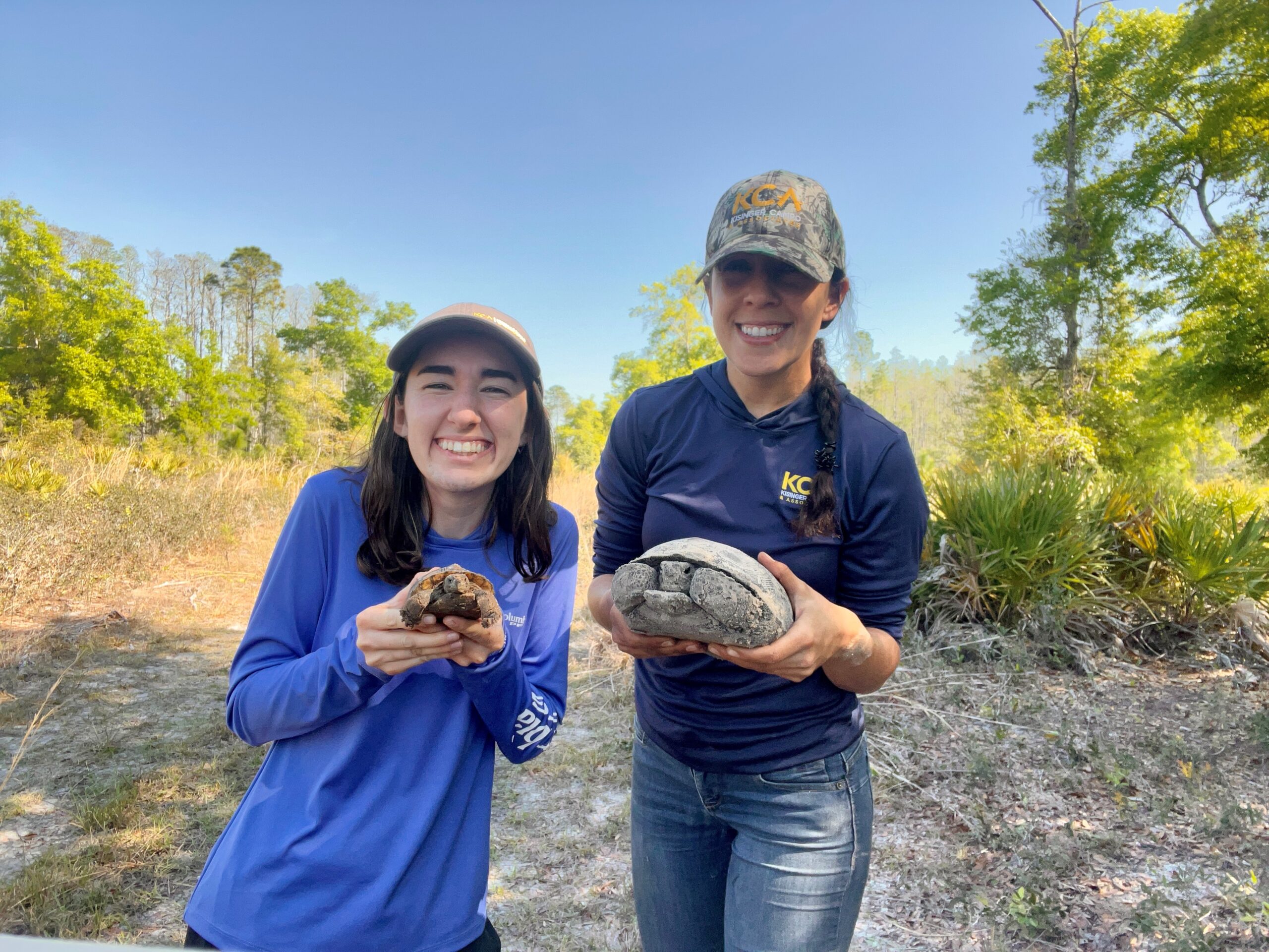 Abdel-Hadi and Gonthier smiling, holding small tortoises in a sunny, wooded area