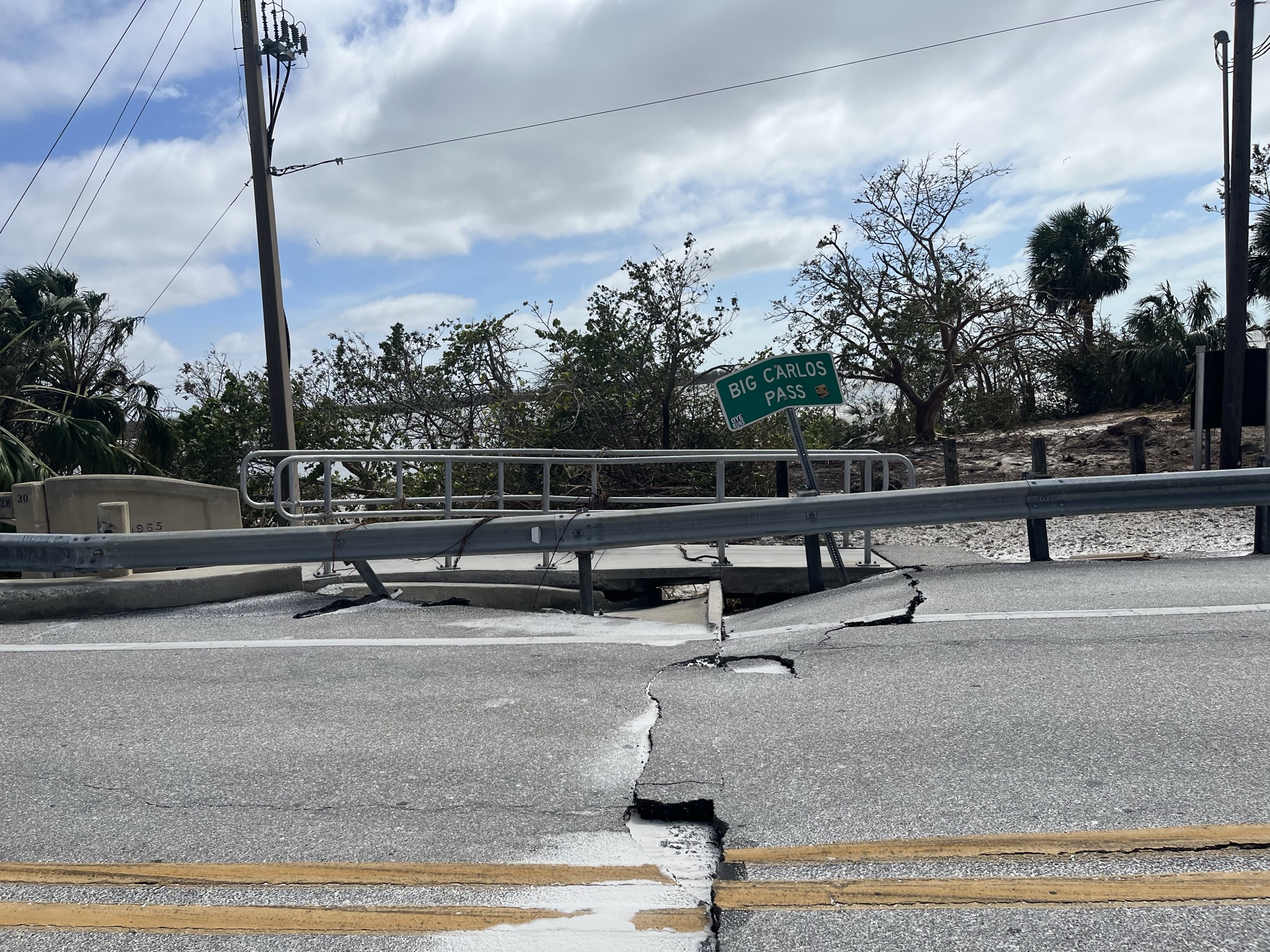 Cracked road near Big Carlos Pass signpost, damaged guardrail, overcast sky