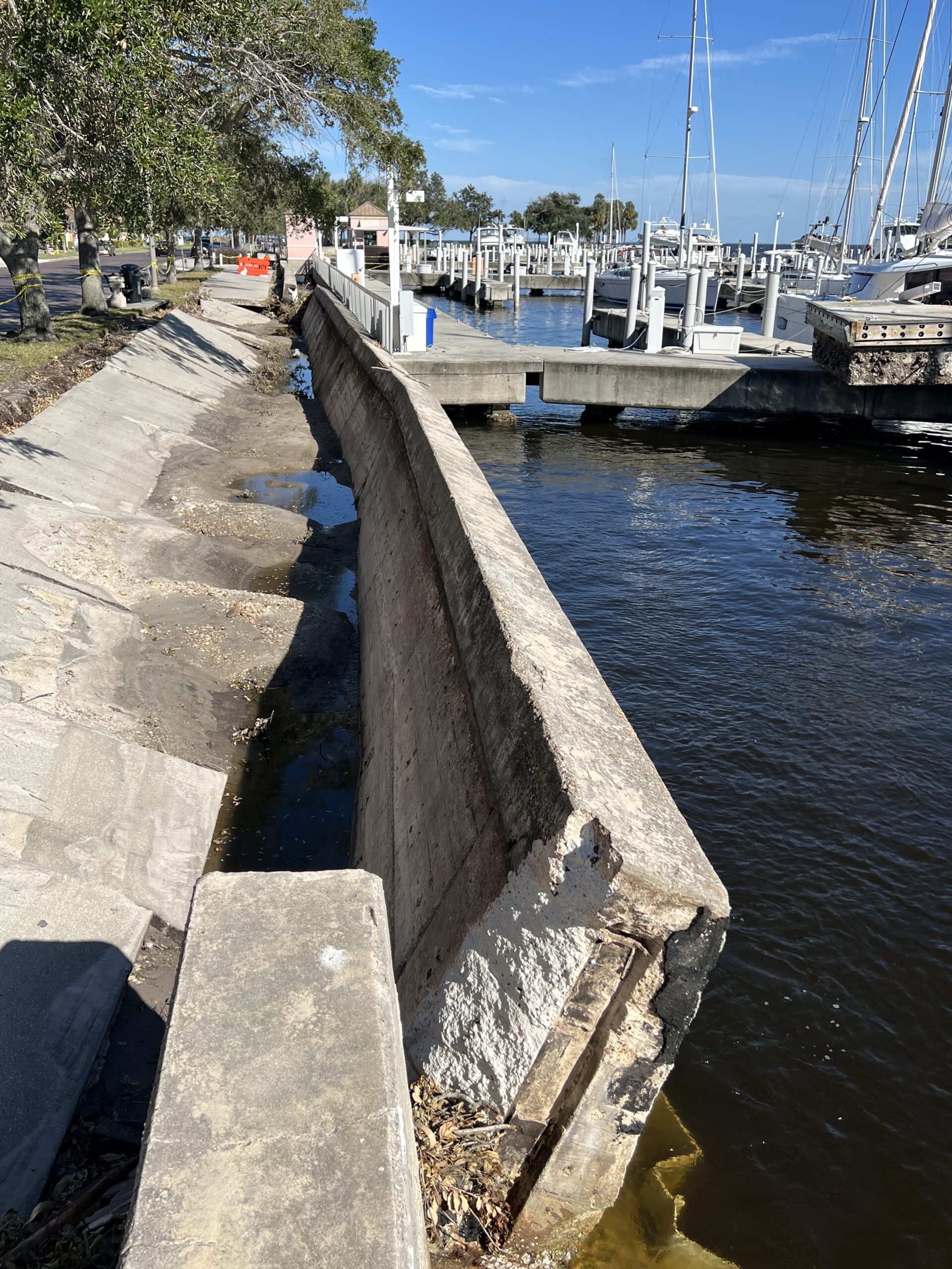 Broken concrete seawall by a marina with boats docked nearby
