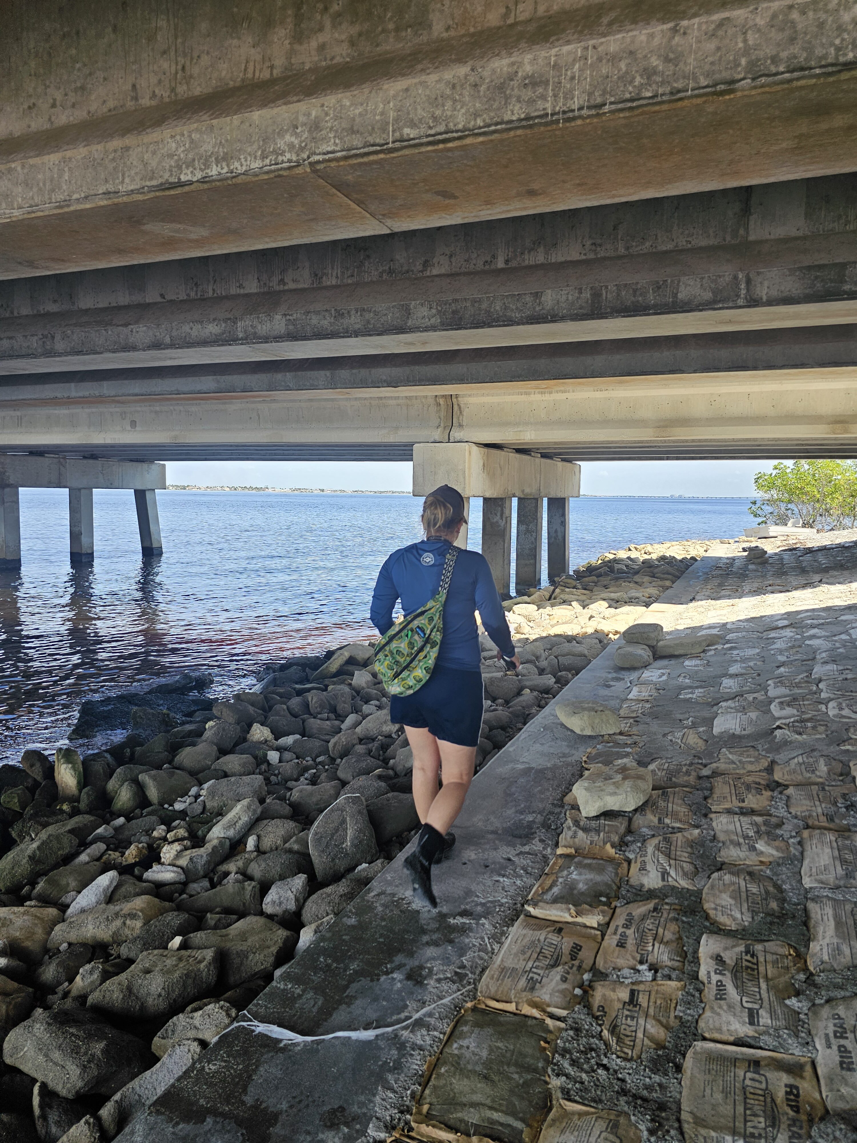 Nicole walking under Cape Coral bridge by rocky waterfront