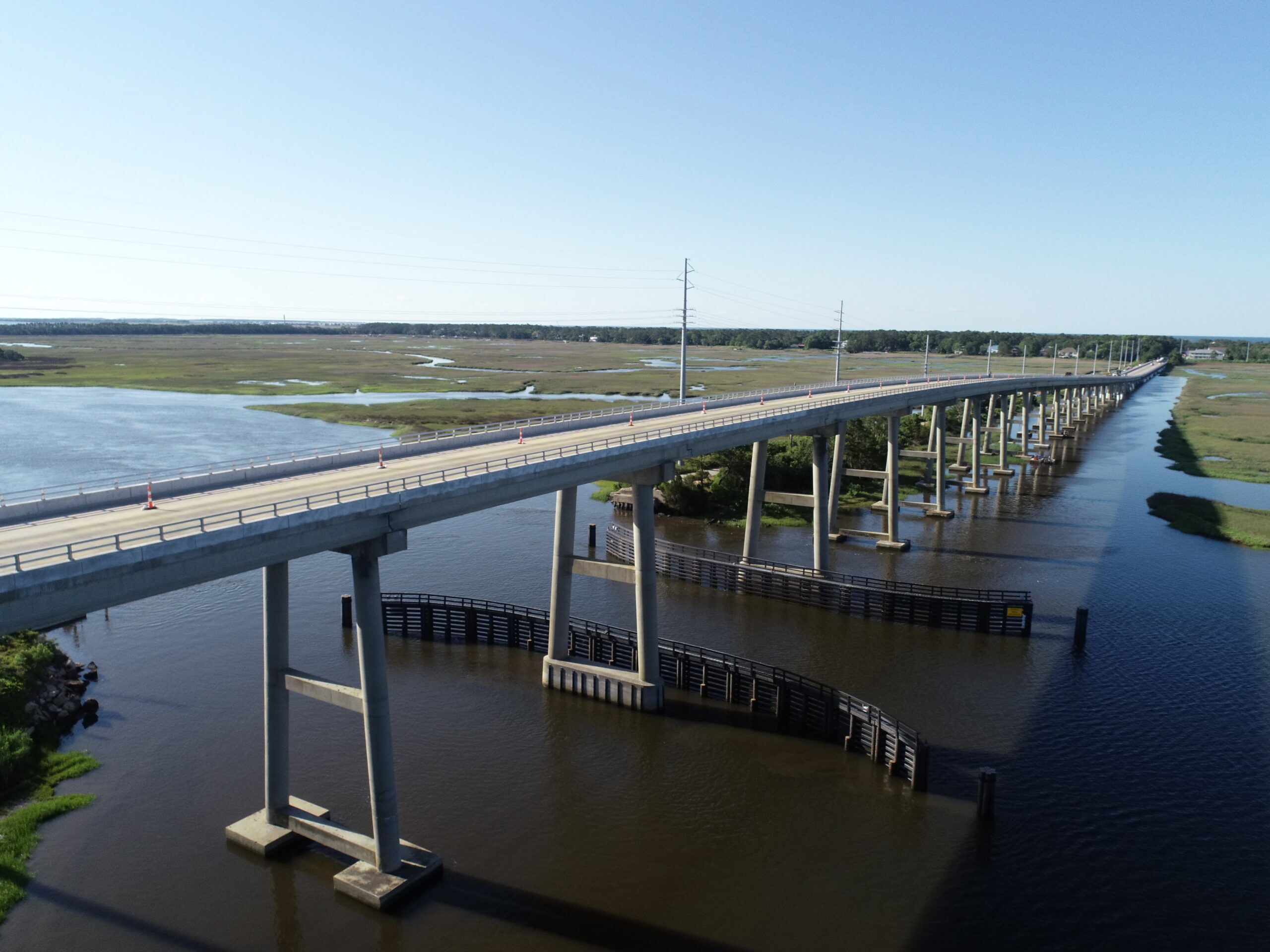 Elevated bridge extending over a wide river; marshland visible beneath clear blue sky