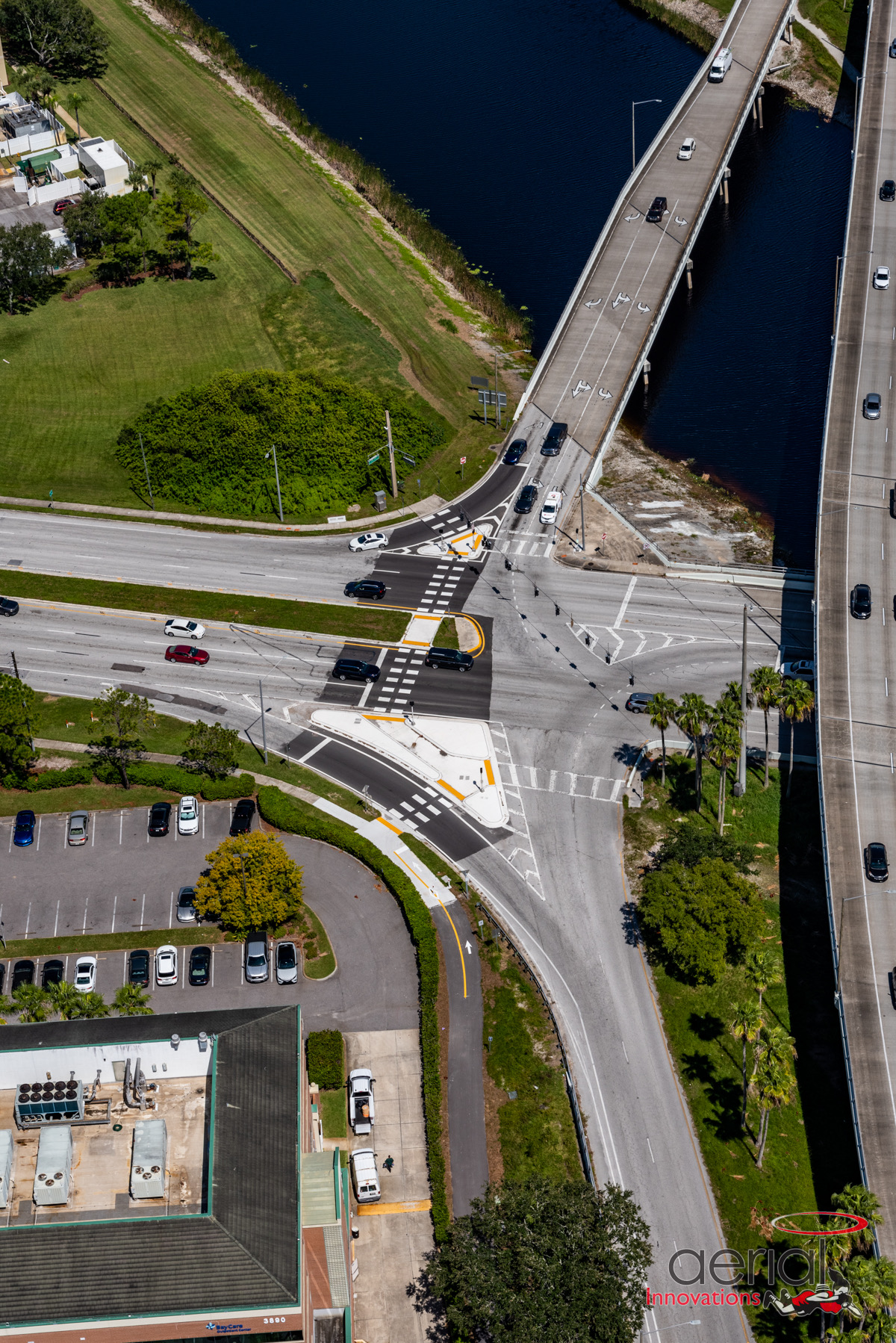 Aerial view of intersecting roads with vehicles, near waterway and green spaces