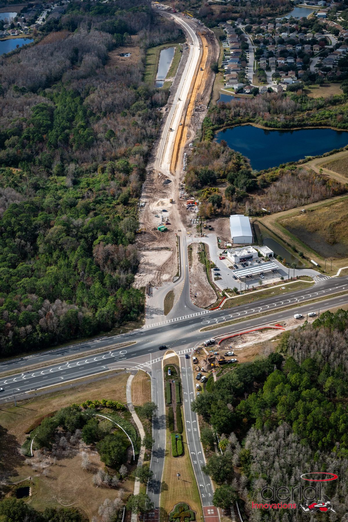 Aerial view of a road construction site through a wooded area alongside residential neighborhood and ponds