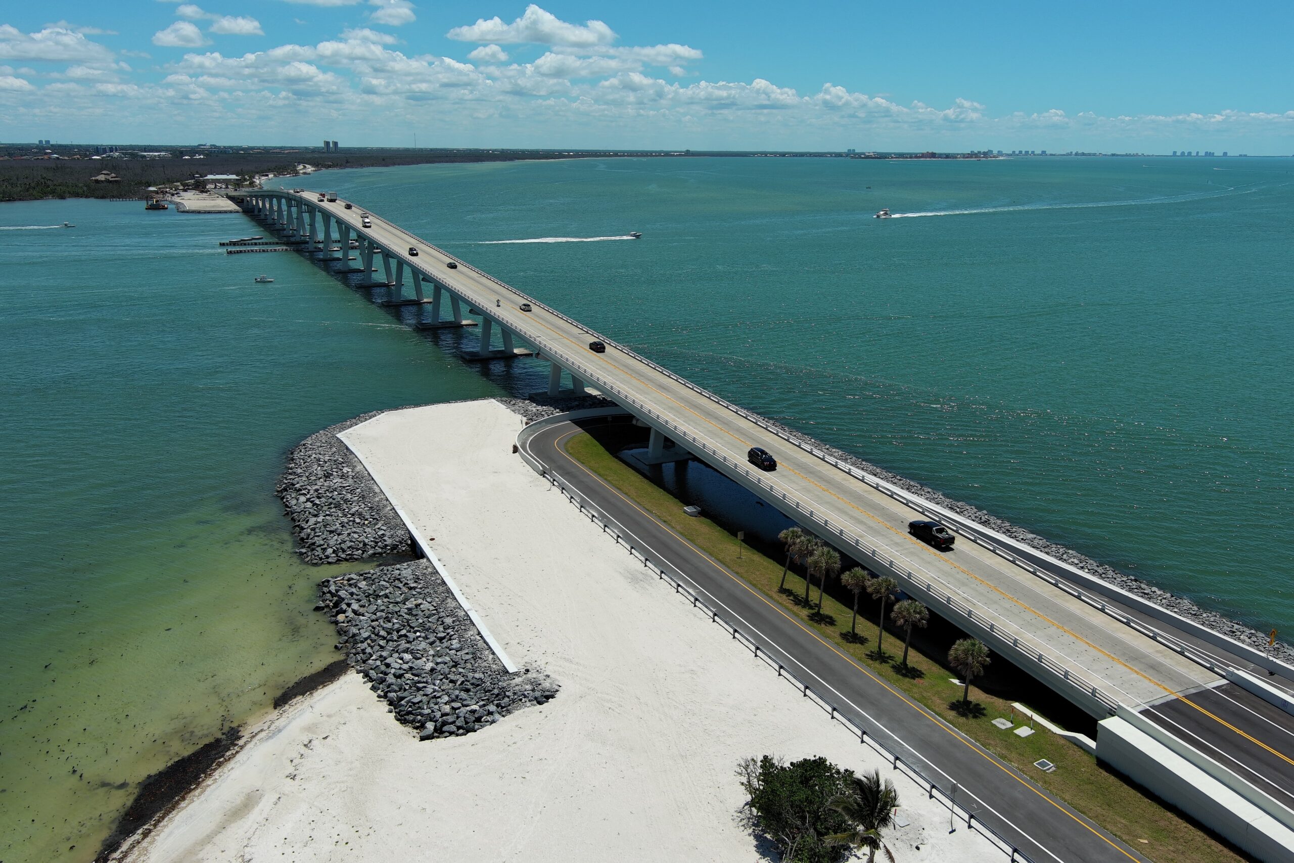 Aerial view of a long bridge over turquoise water, connecting land with cars crossing