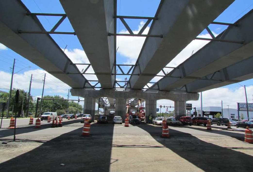 View under steel bridge construction, traffic cones, and vehicles below