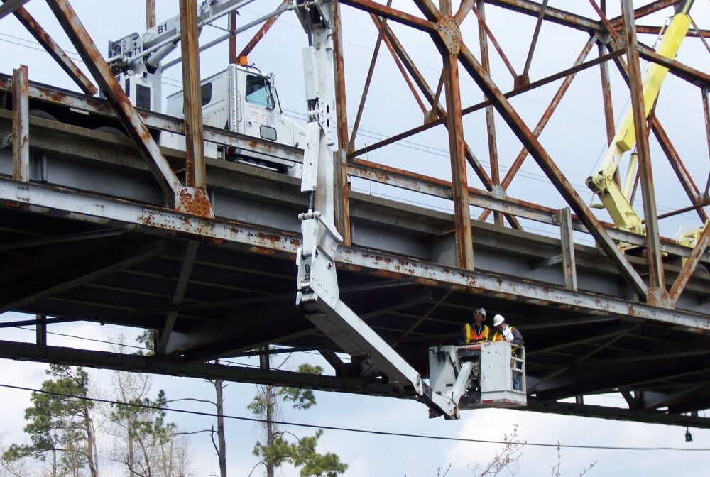 Workers inspecting bridge underside using hydraulic lift platform