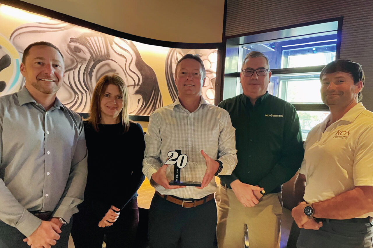 Group of five people smiling with one holding a "20 Years" award