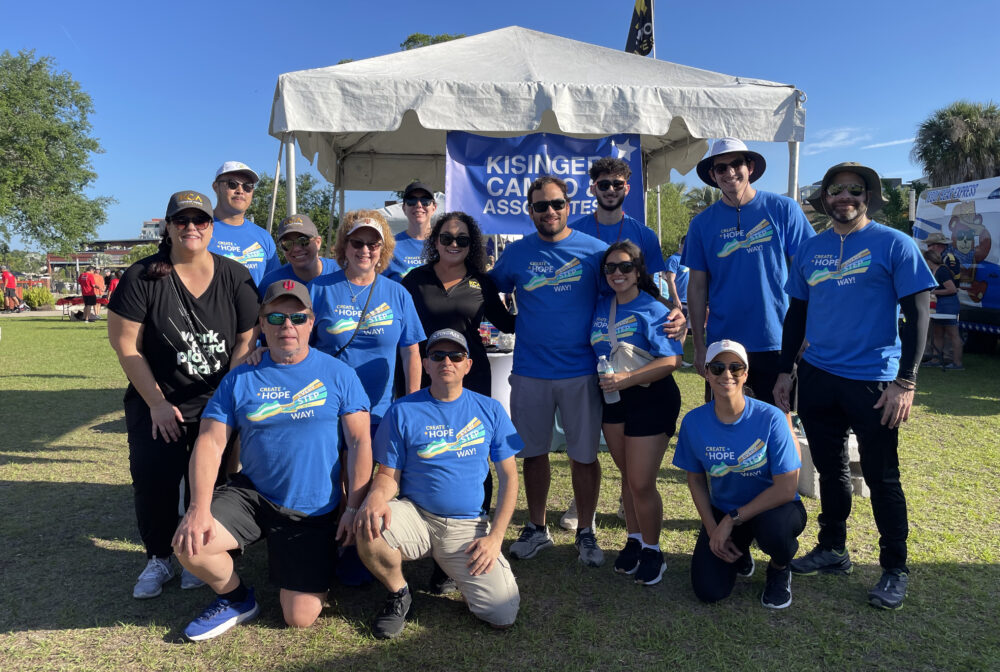 Group of people in blue "Create Hope" shirts at a charity event, smiling in front of a tent in a sunny park