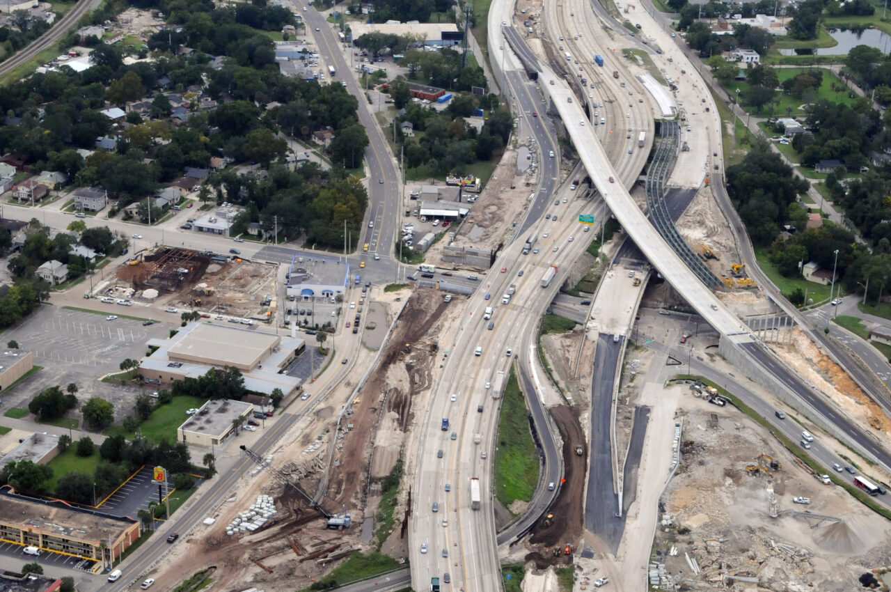 Aerial view of a multi-lane highway under construction, with intersecting roads and surrounding urban area