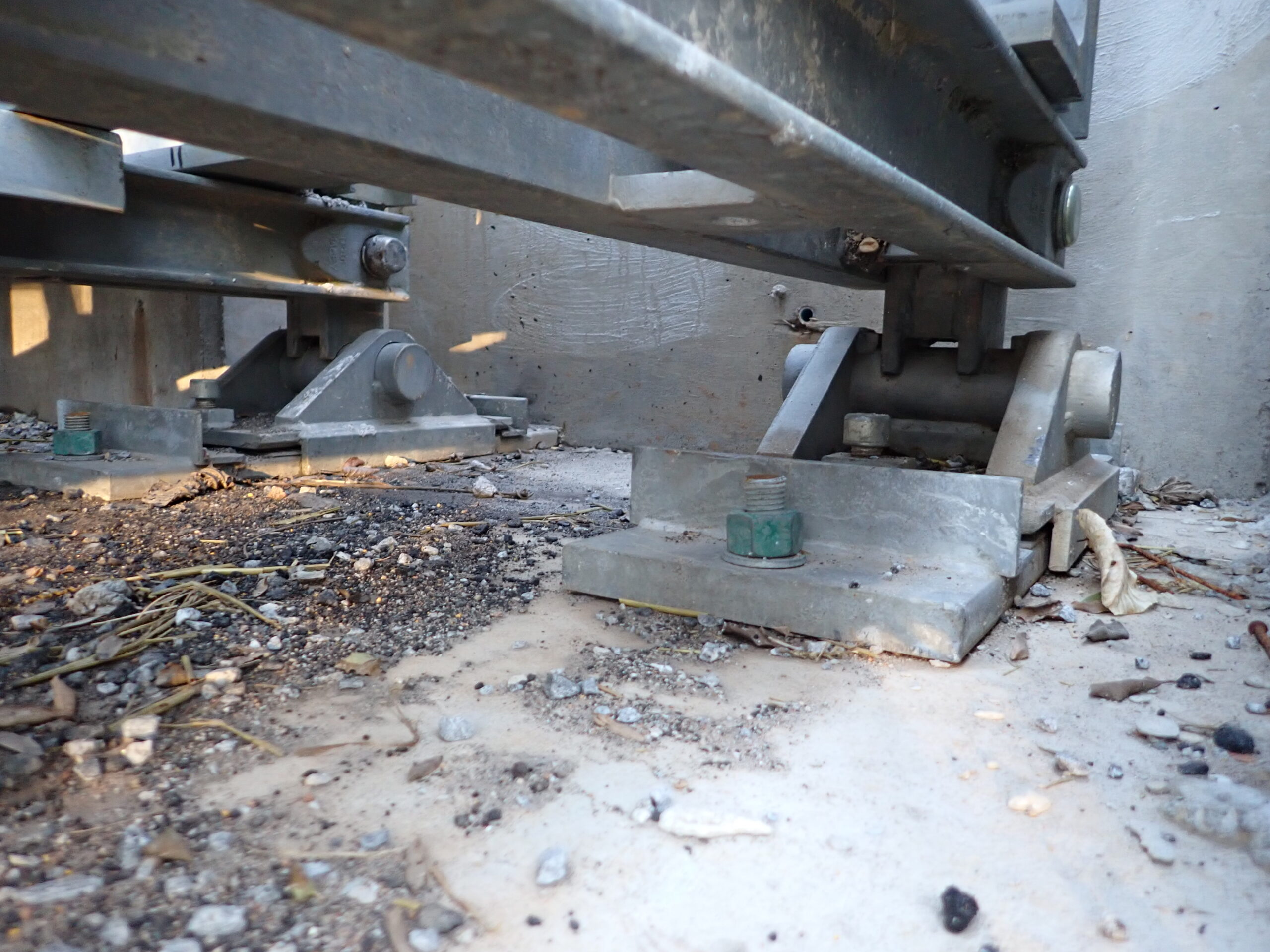 Structural movable bearings supporting a metal beam, surrounded by dirt and debris