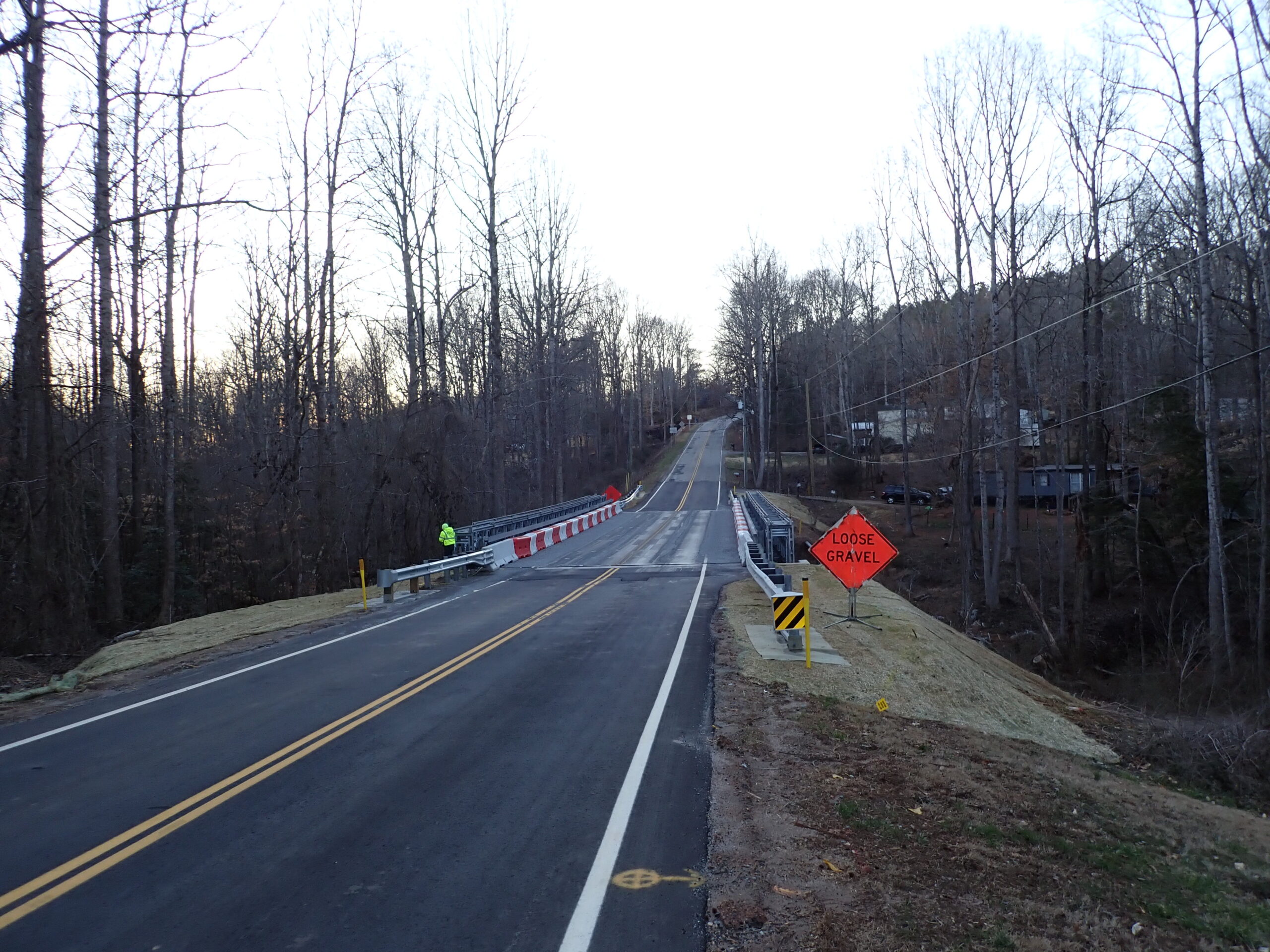 Rural road with 'Loose Gravel' sign and bare trees lining the sides