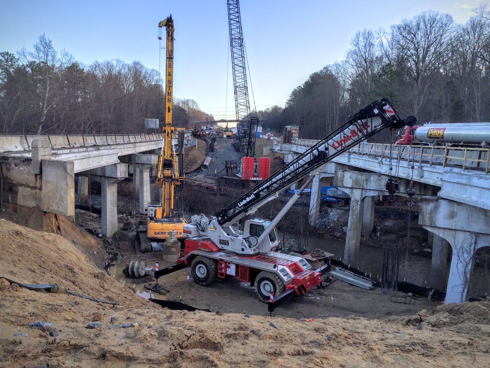 Construction site with heavy machinery and cranes working on a bridge project over a muddy area