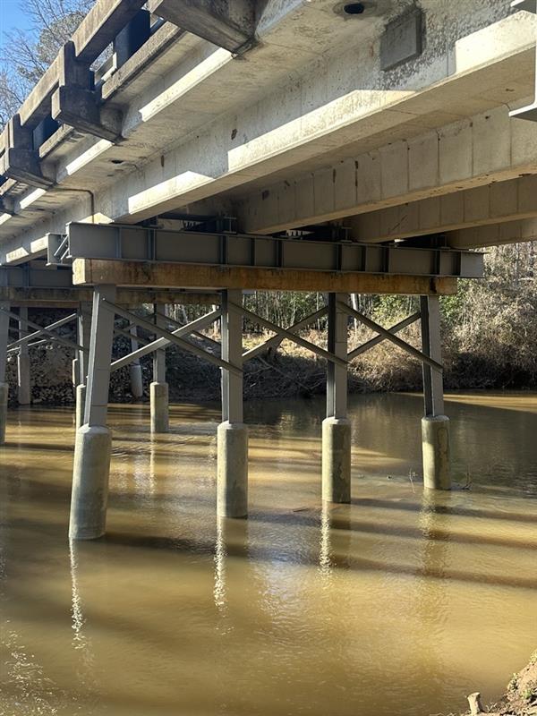 Underneath a concrete bridge with metal supports over a muddy river