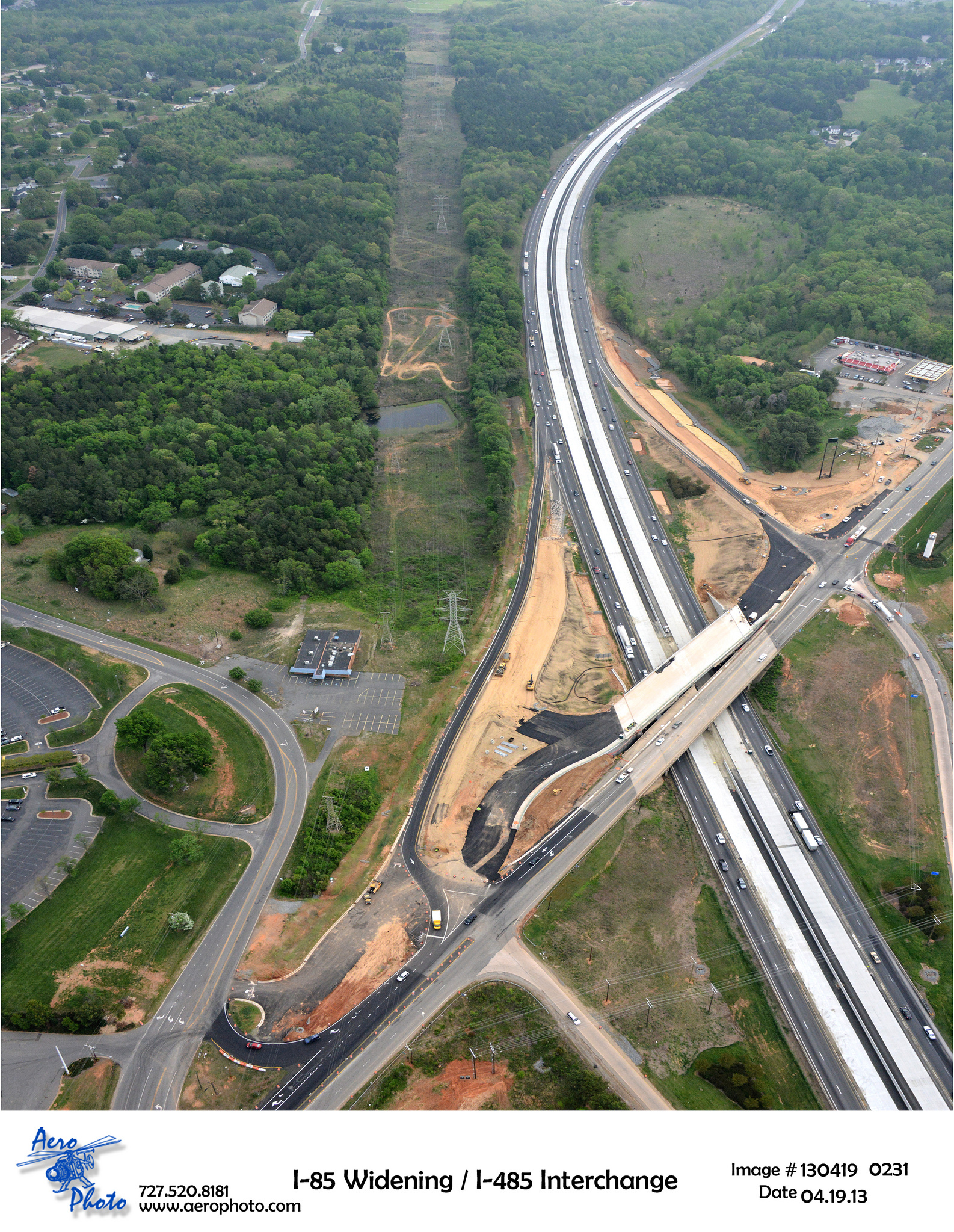 Aerial view of I-85 and I-485 interchange construction amidst greenery and residential areas; "I-85 Widening / I-485 Interchange" text