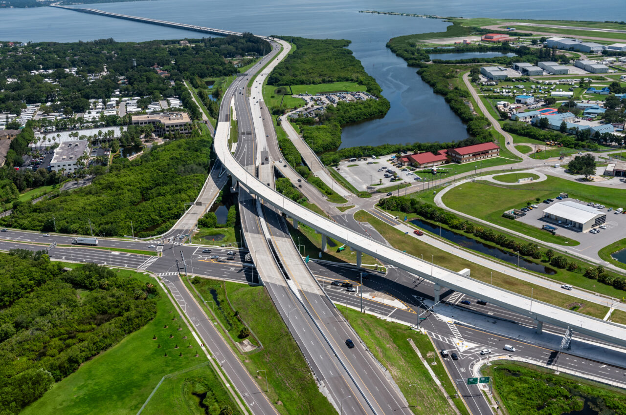 Aerial view of elevated roadway with intersecting highways, surrounded by greenery and buildings near a waterway