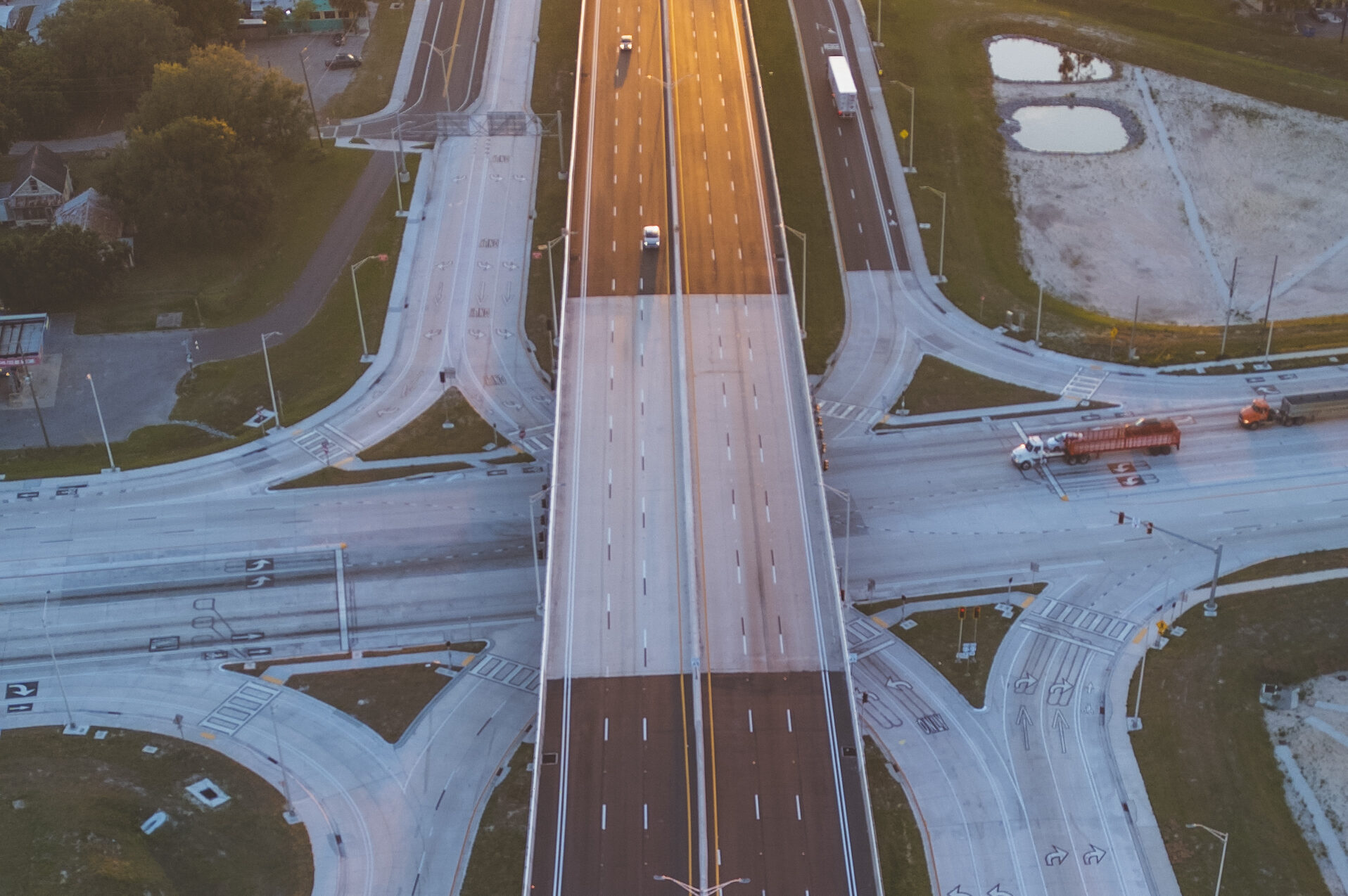 Aerial view of a highway interchange at sunset with traffic and intersections, surrounded by trees and buildings