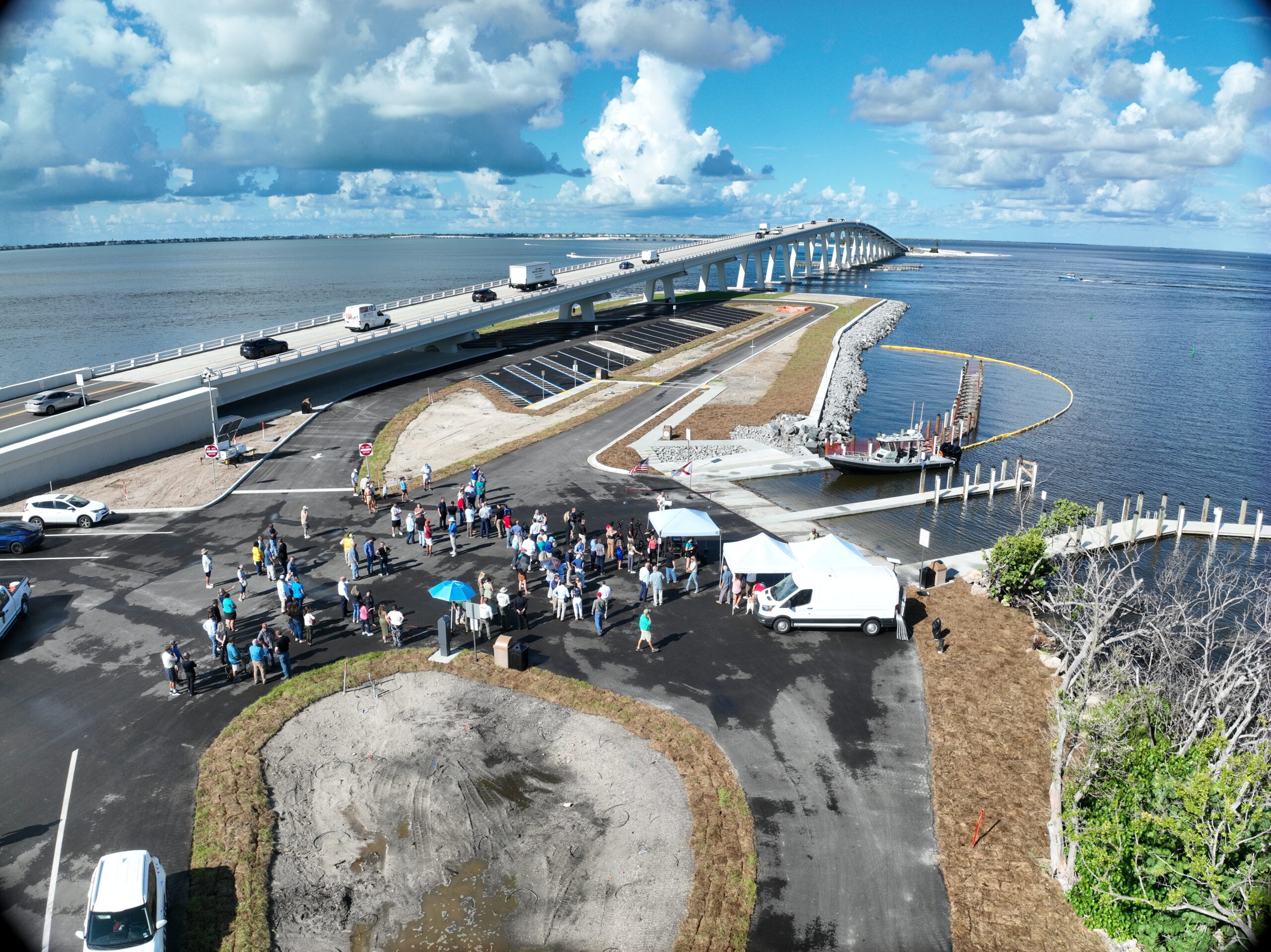 Crowd gathers near a new bridge over a large body of water, under a partly cloudy sky
