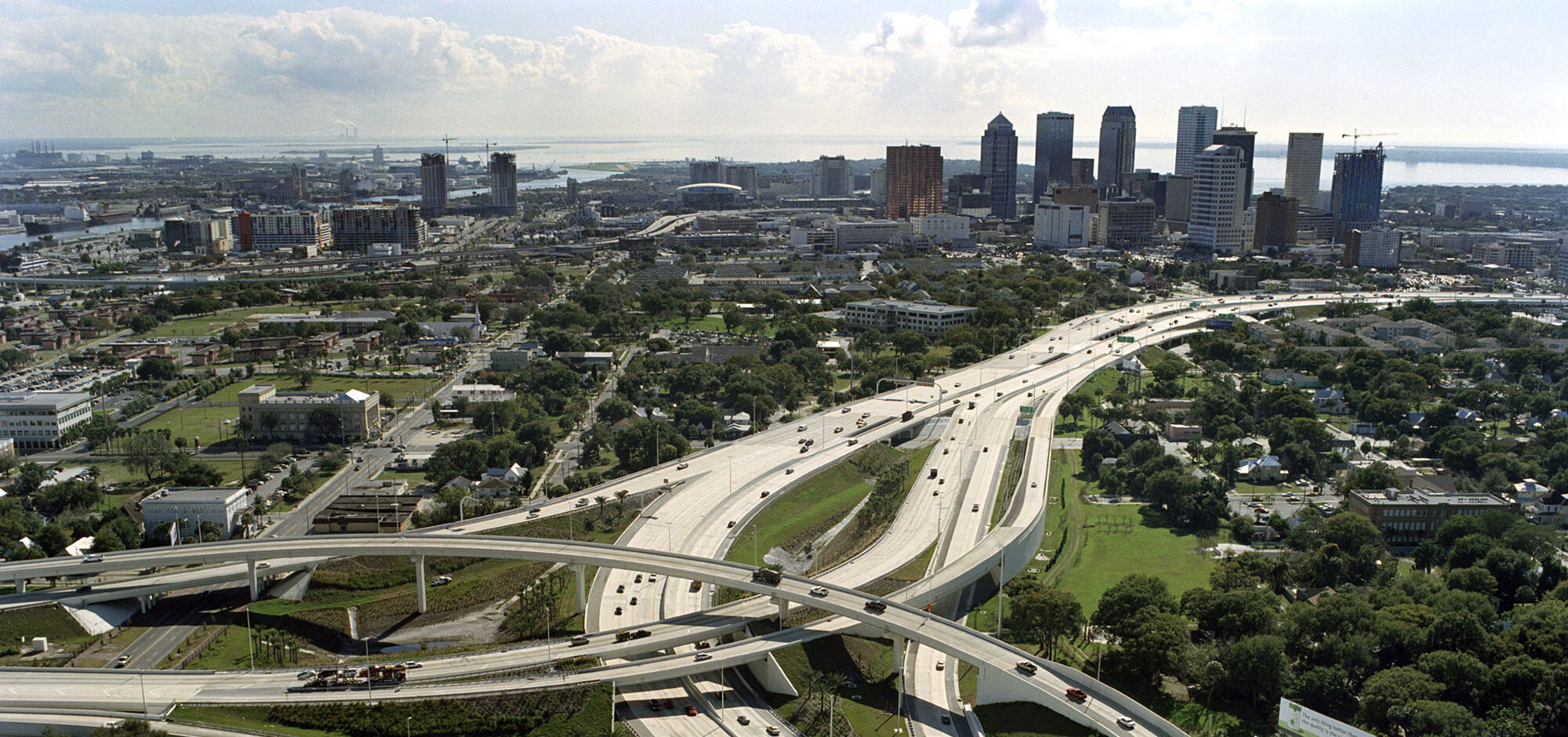 Aerial view of highway interchange with vehicles amid urban skyline and green spaces