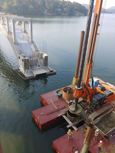 Construction workers operating machinery on a bridge pier over water