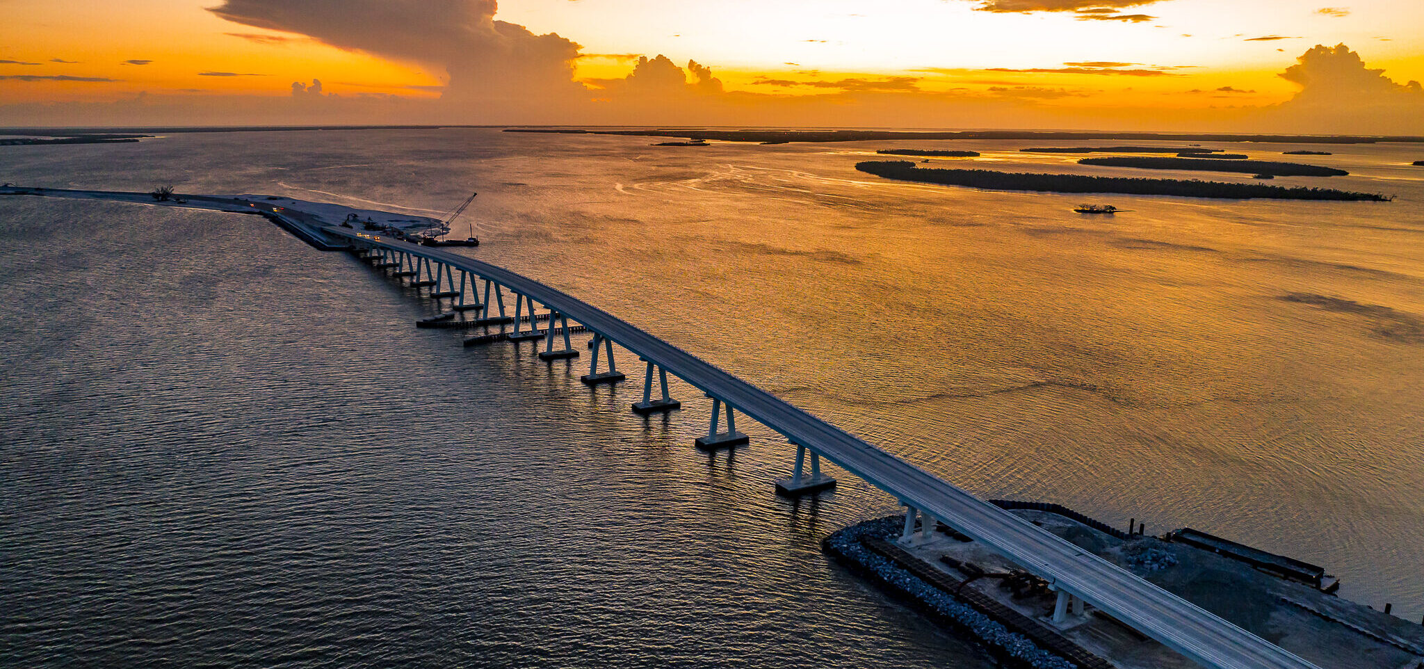 Bridge stretching over water at sunset with orange sky