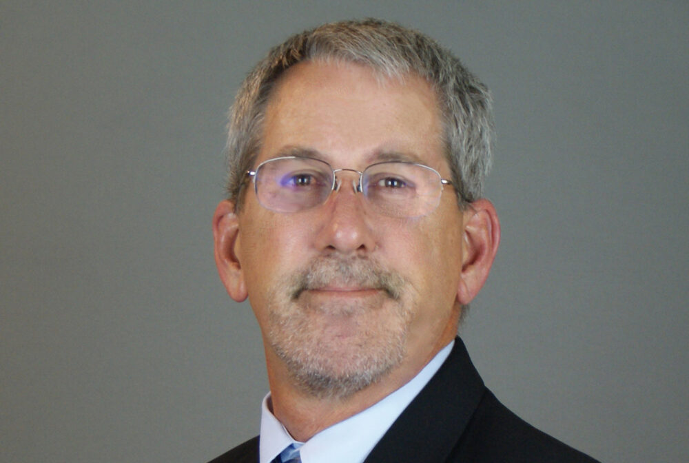 Foley in a suit smiling slightly against gray background