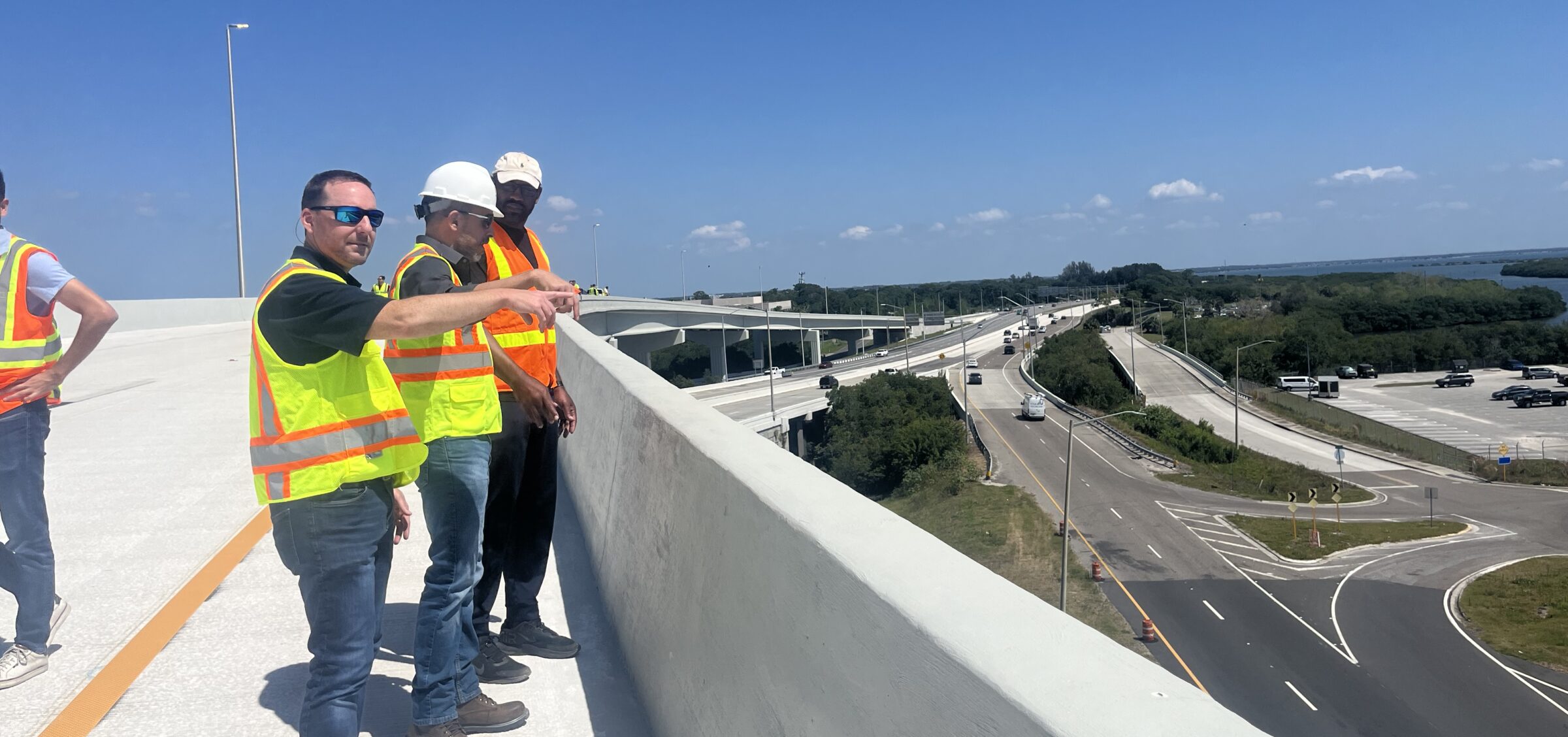 People in construction gear inspecting highway from overpass, clear sky background