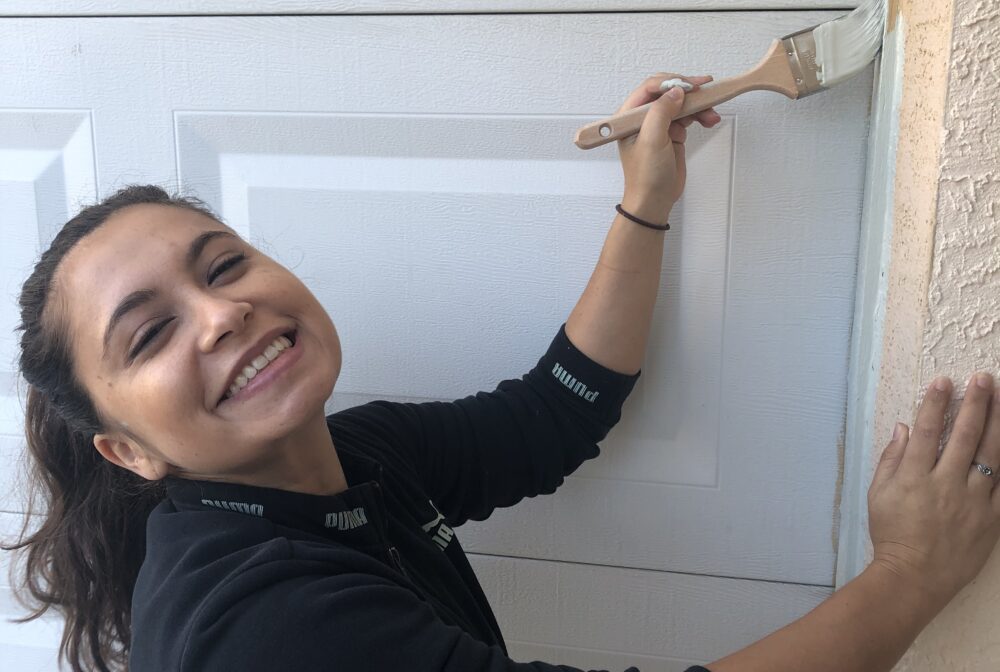 IMG_1509.jpg depicts a smiling person painting a garage door edge white