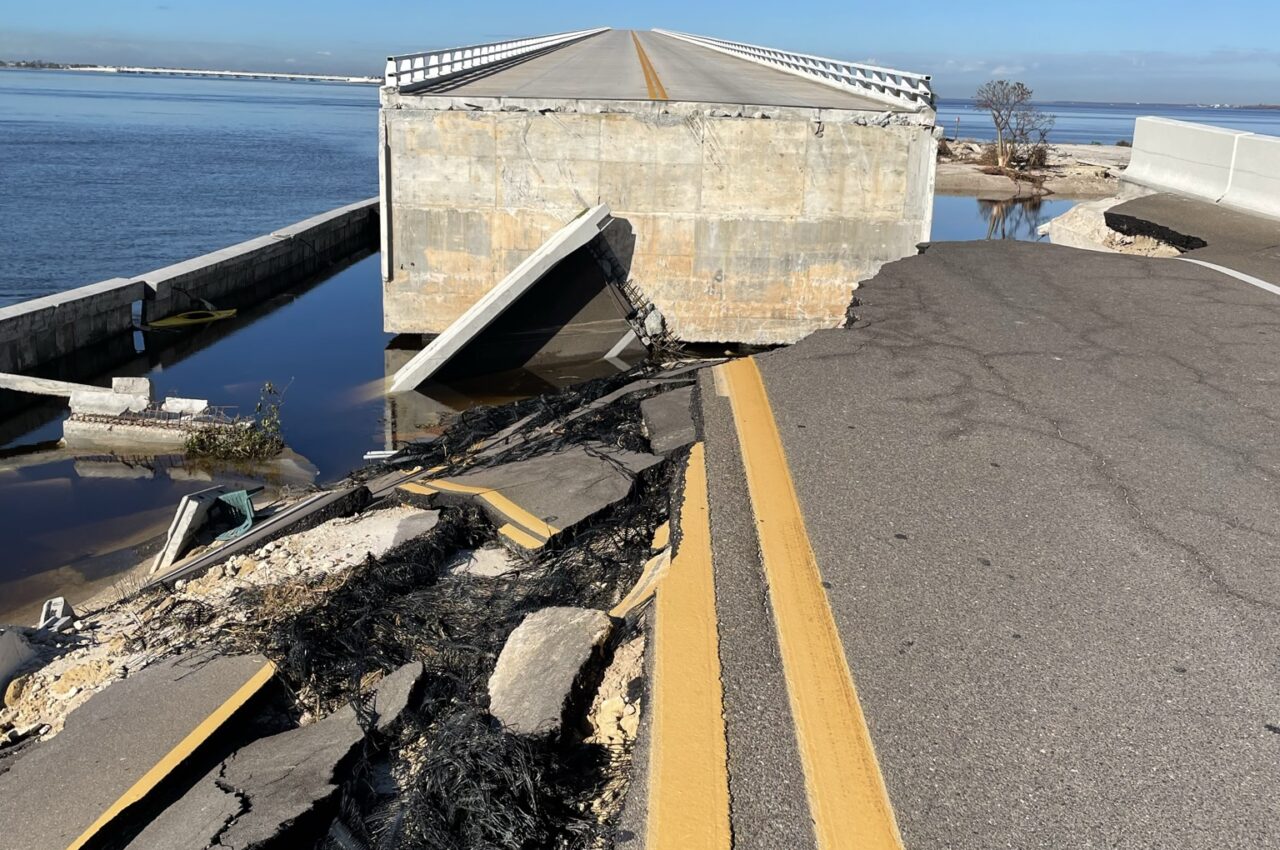 Collapsed Sanibel Causeway with fractured road and exposed debris by a body of water