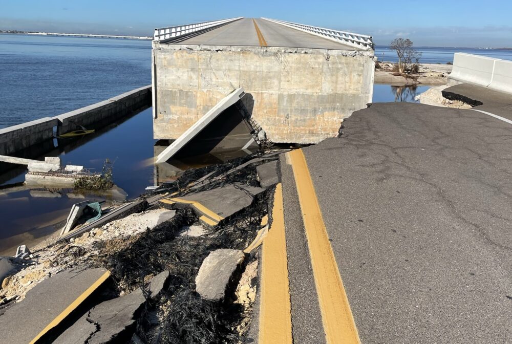 Collapsed Sanibel Causeway with fractured road and exposed debris by a body of water