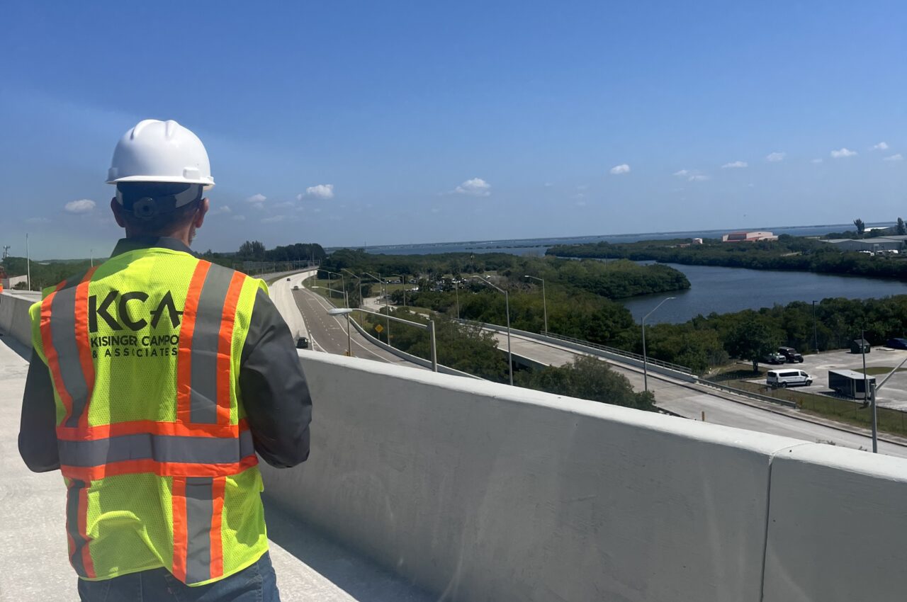 Person in hard hat and KCA vest overlooking highway and river