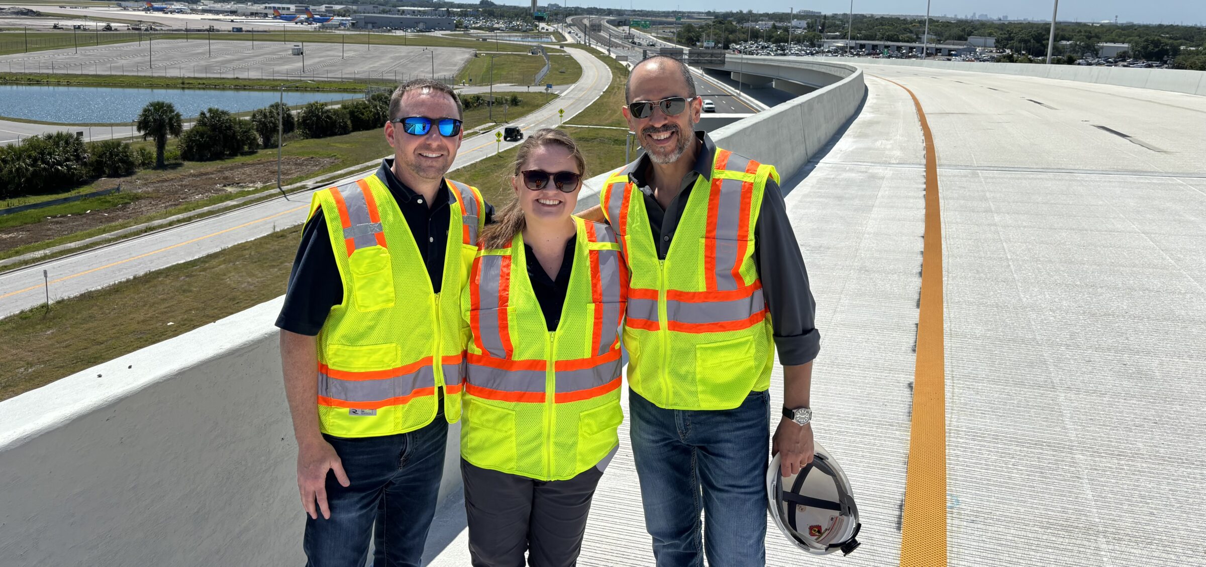 Three people in safety vests smiling on a highway overpass