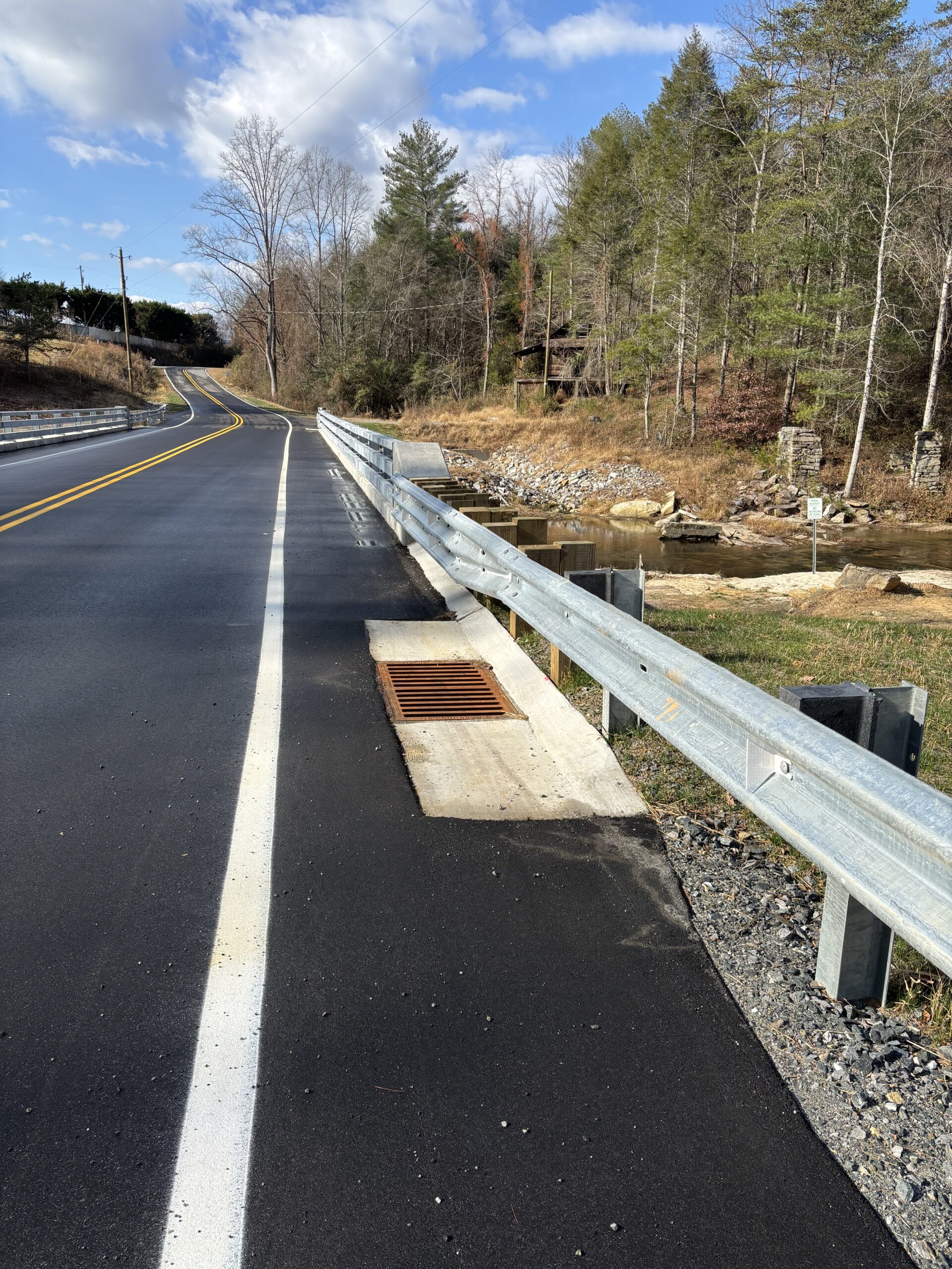 Roadside with metal guardrail and drainage grate, trees lining one side