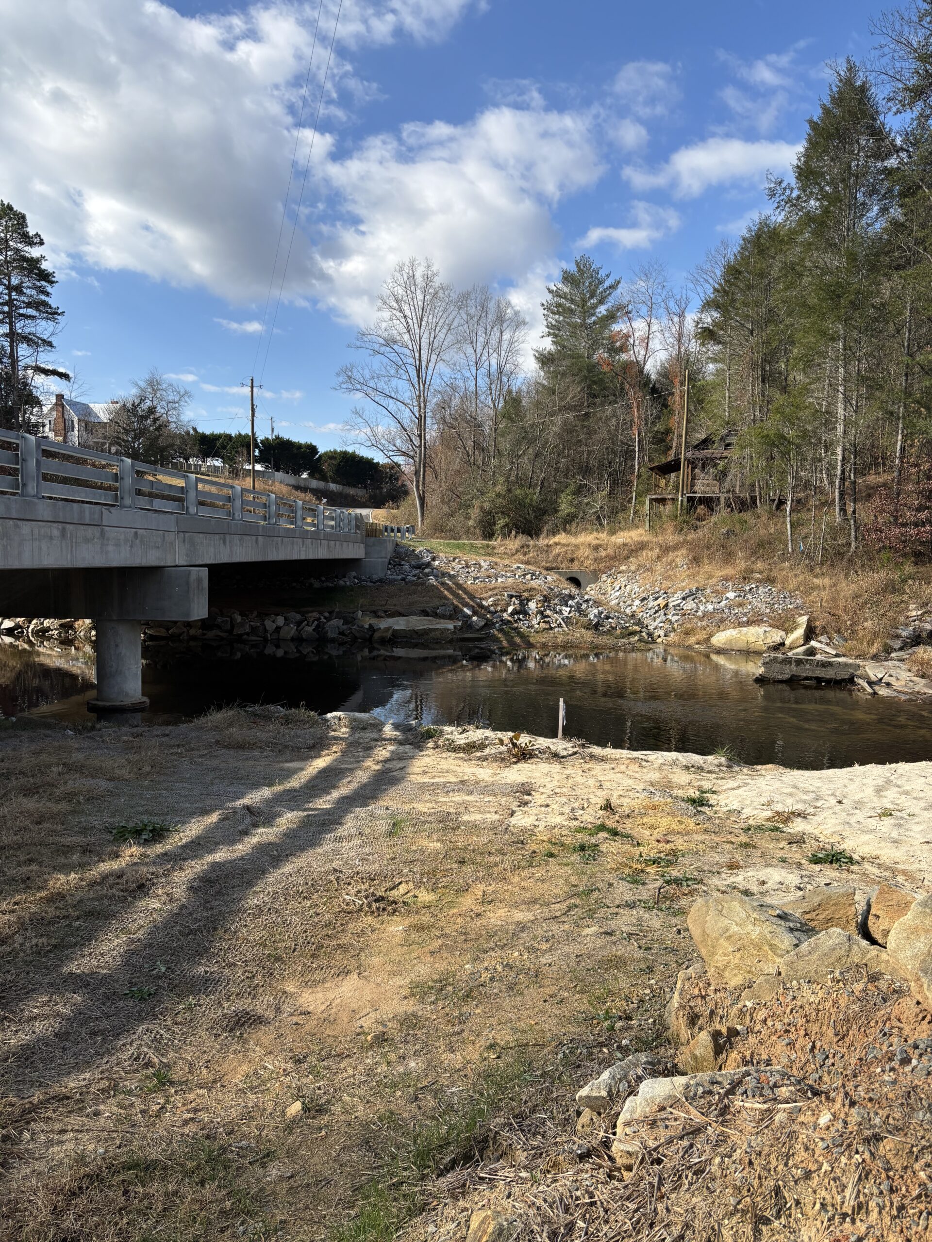 Bridge over a small, rocky river with surrounding trees under a blue sky