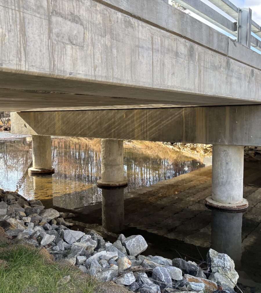 Concrete bridge over a river with rocky embankment and clear reflections