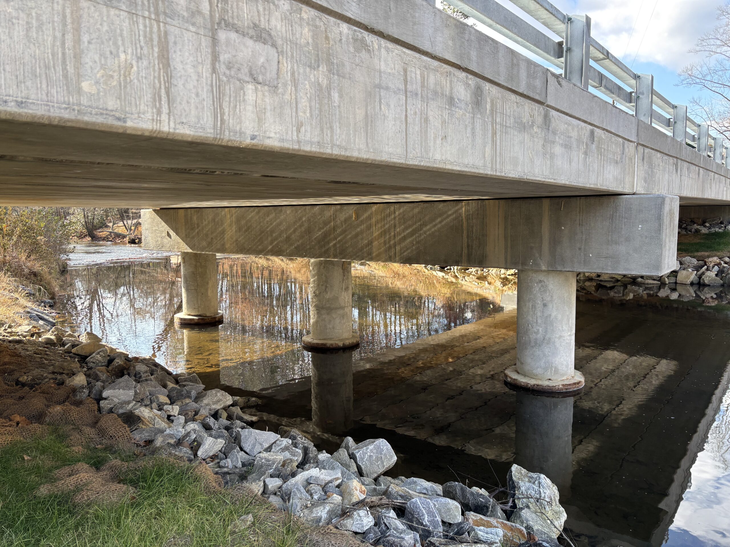 Concrete bridge over a river with rocky embankment and clear reflections