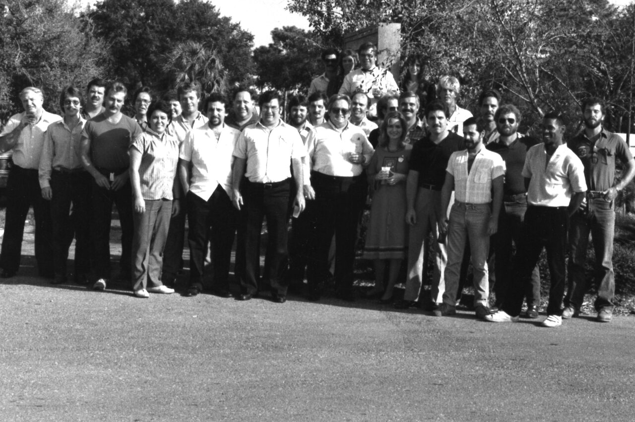 Group of people standing outdoors, smiling, casual dress, trees in background