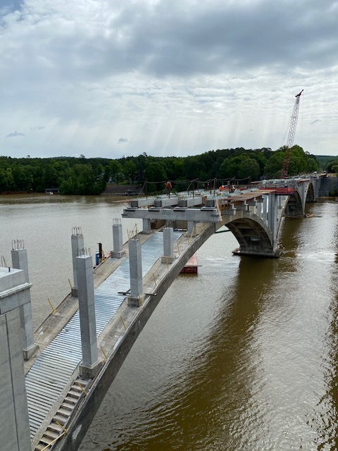 Bridge under construction over a river with crane and cloudy sky