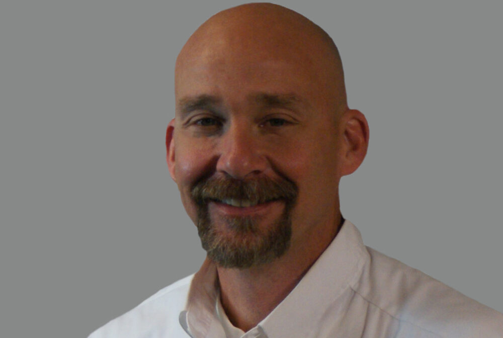 Patrick smiling in a white shirt with KCA logo