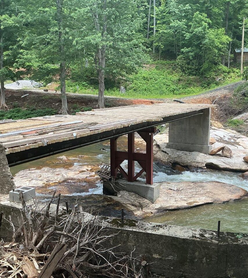 Wooden bridge over a flowing stream surrounded by lush green forest