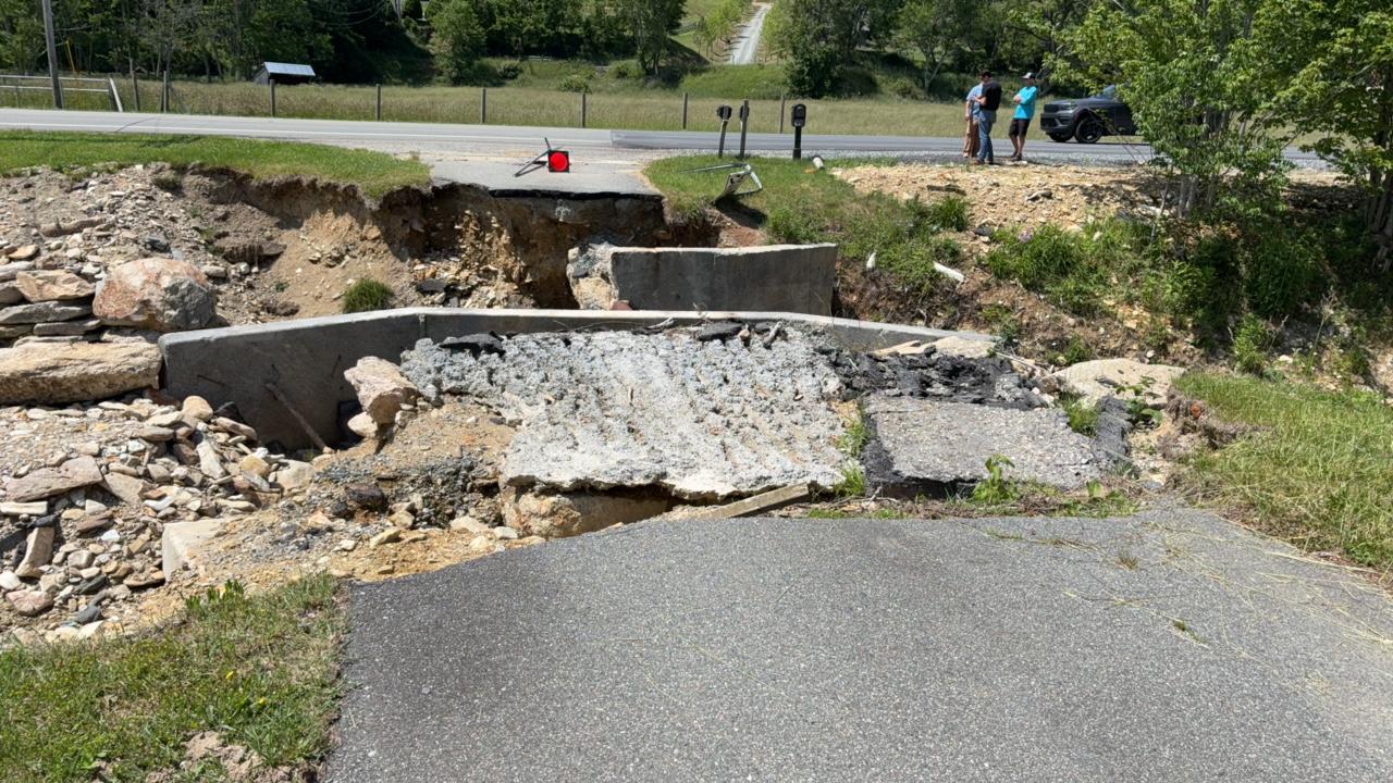Collapsed road with exposed rubble, two people observing, car nearby