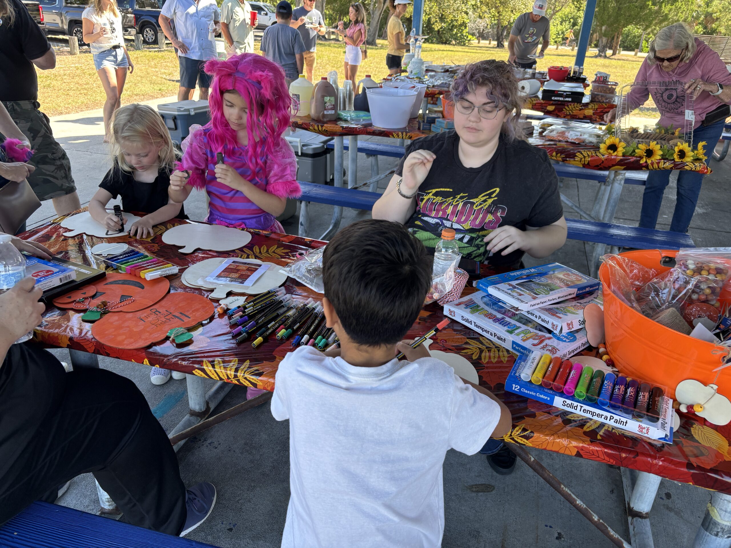 Children and adults at a picnic table doing arts and crafts activities with markers and paints